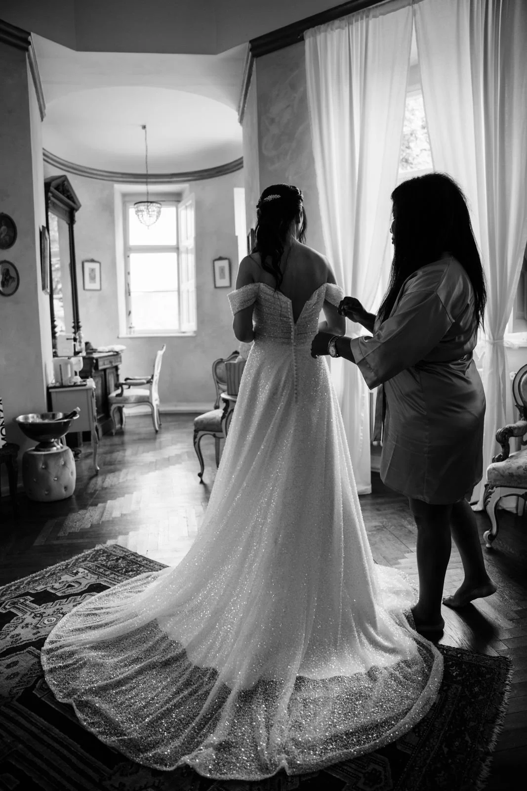 Eine Braut wird von einer Frau in einem eleganten Raum mit antiken Möbeln für ihren Hochzeitstag vorbereitet.