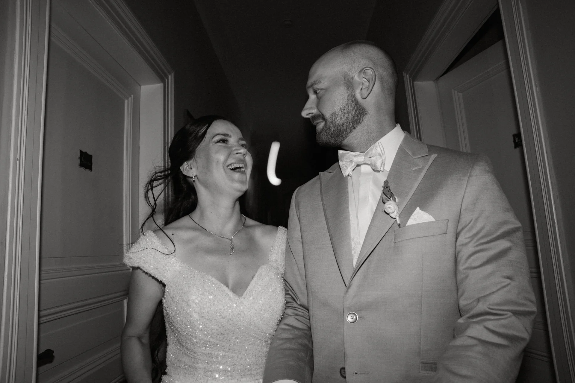 Braut und Bräutigam lachen sich an, stehen in einer Flur bei einer Hochzeit, schwarz-weiß Foto.