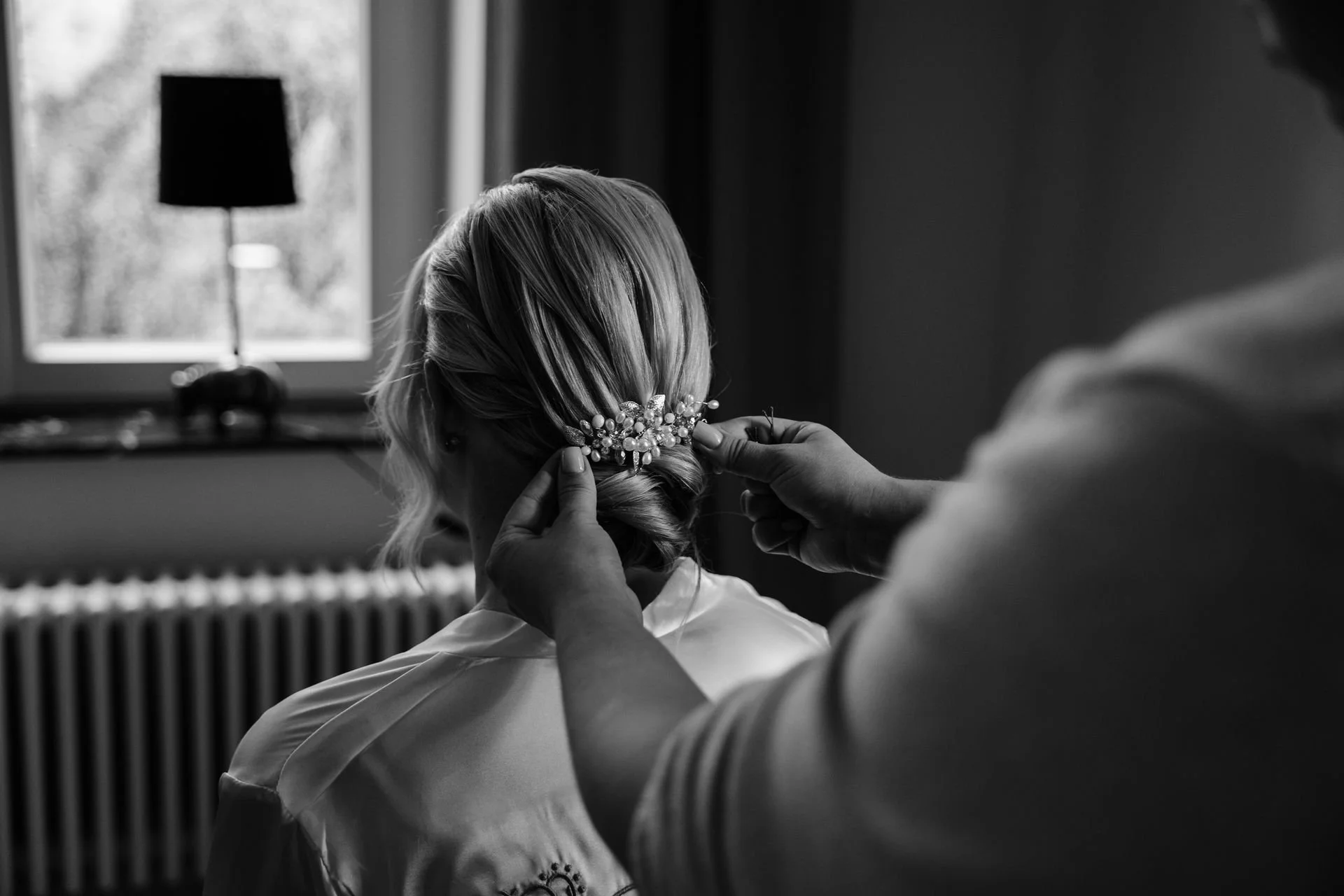 Eine Braut wird vor ihrer Hochzeit von einer Person mit einem Haarkamm mit Perlen und Blumen geschmückt.