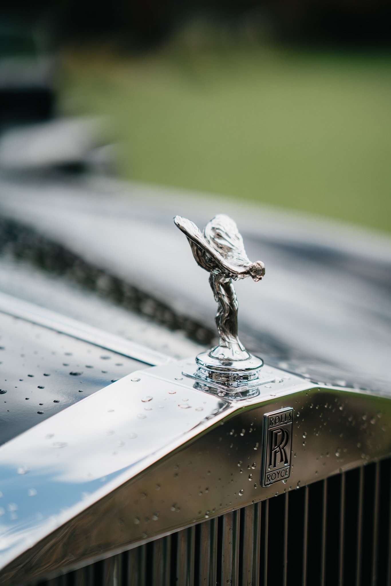 Nahaufnahme des Autokennzeichens von einem Rolls-Royce, mit Wassertröpfchen auf der Motorhaube und dem ikonischen Spirit of Ecstasy Ornament.