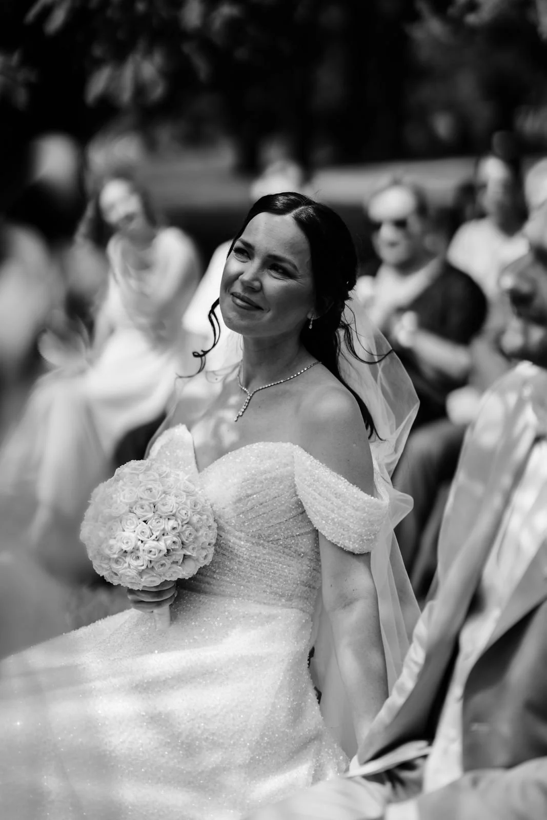 Braut mit dunklem Haar in weißem Hochzeitskleid hält einen Blumenstrauß bei einer Hochzeit im Freien.