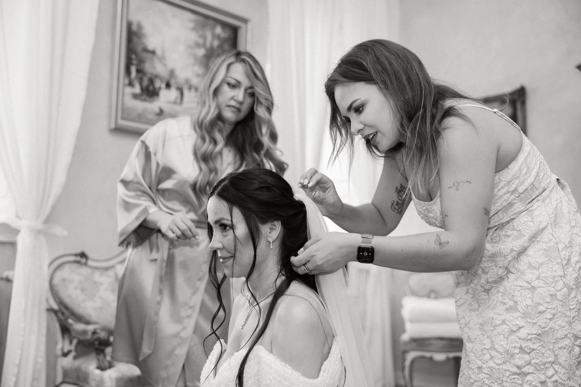 Drei Frauen bereiten eine Braut im Zimmer mit antiken Möbeln für ihre Hochzeit vor, eine schmückt das Haar der Braut, eine beobachtet, während die dritte steht.