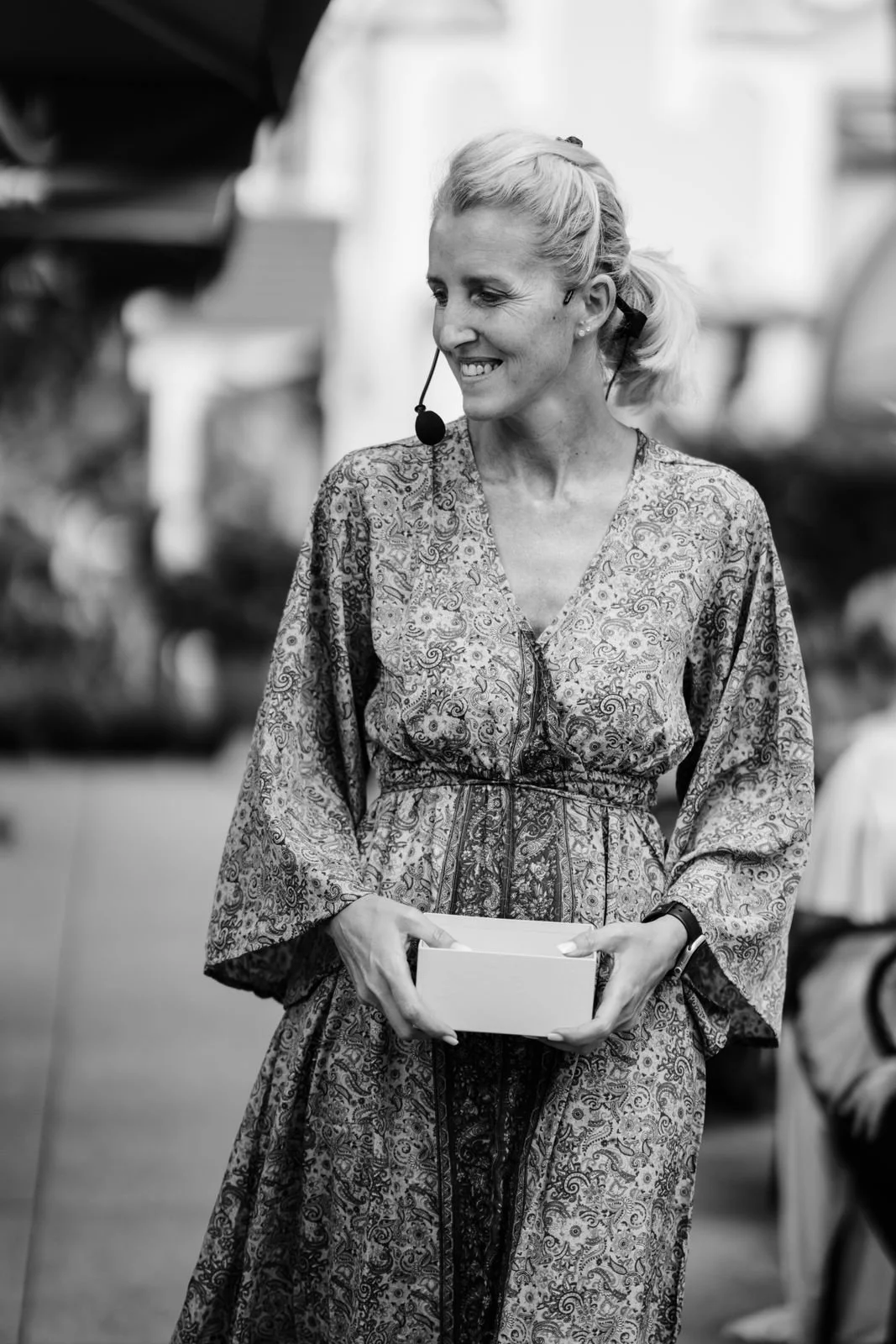 Schwarz-weiß-Foto einer lachenden Frau mit einem Headset, die eine Schachtel in den Händen hält.