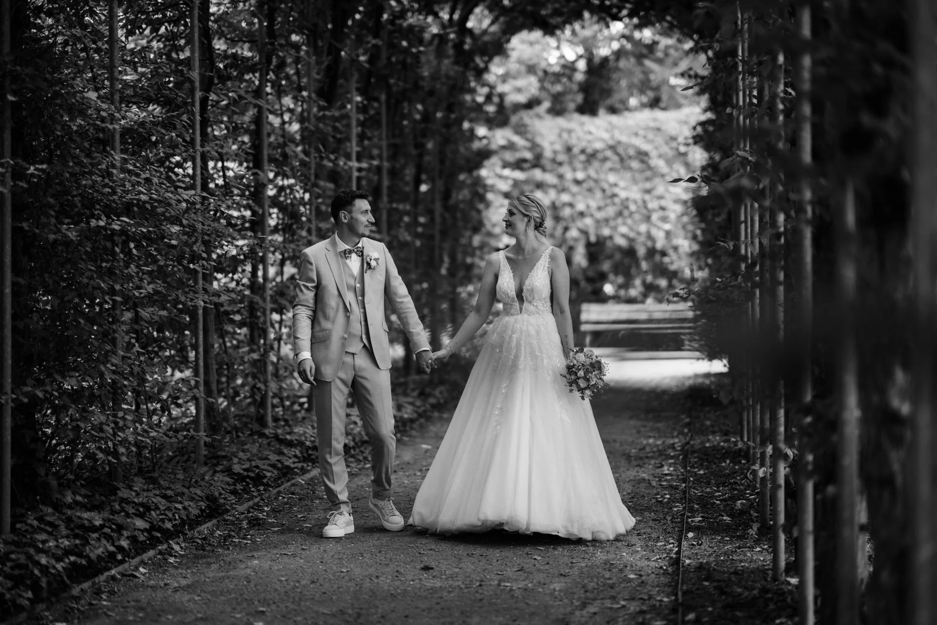 Ein Brautpaar hält Händchen auf einem Waldweg bei einer Hochzeitsaufnahme, schwarz-weiß.