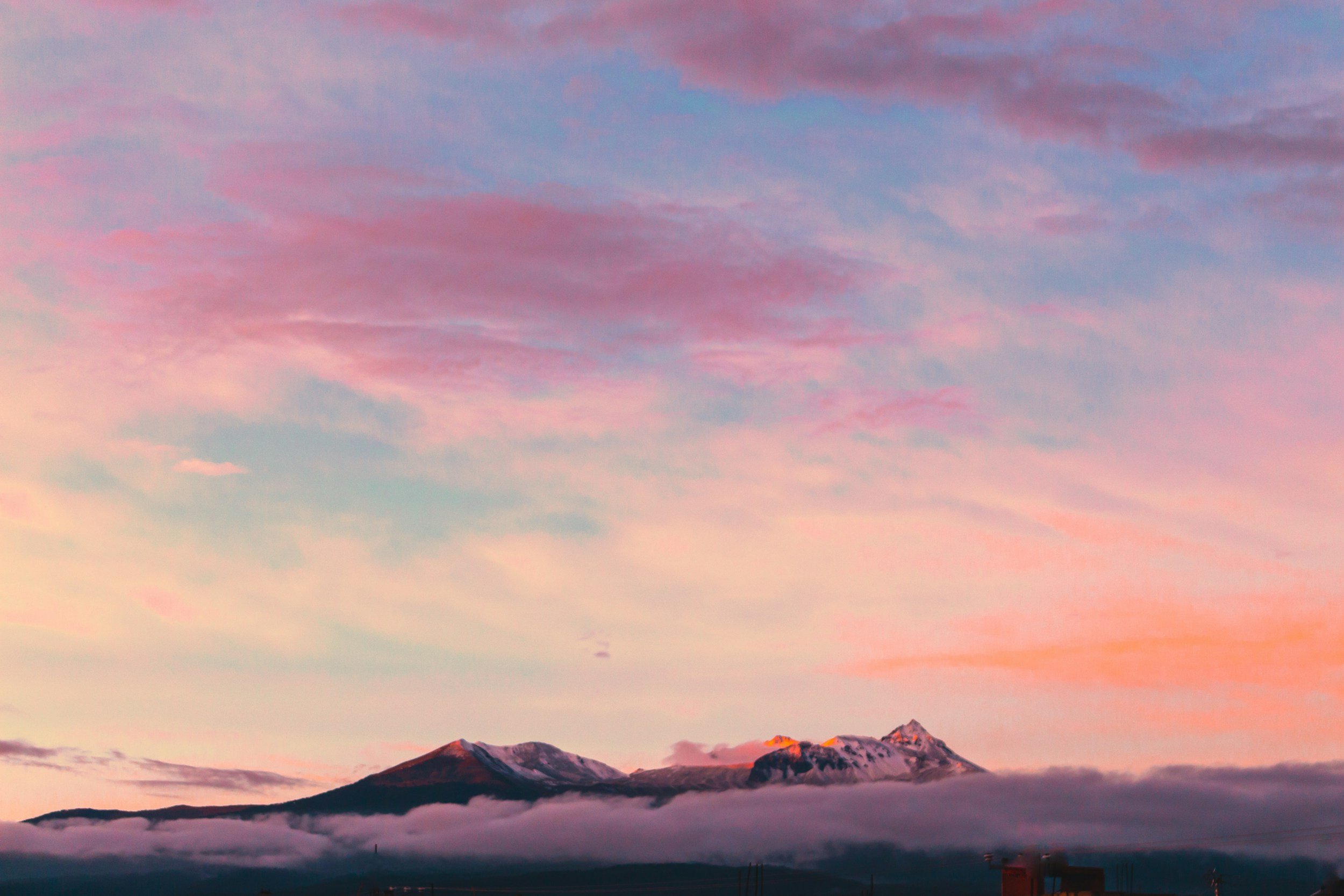 Snow-capped mountains under a colorful, pink and purple sky with layers of clouds and fog at the base of the mountains.