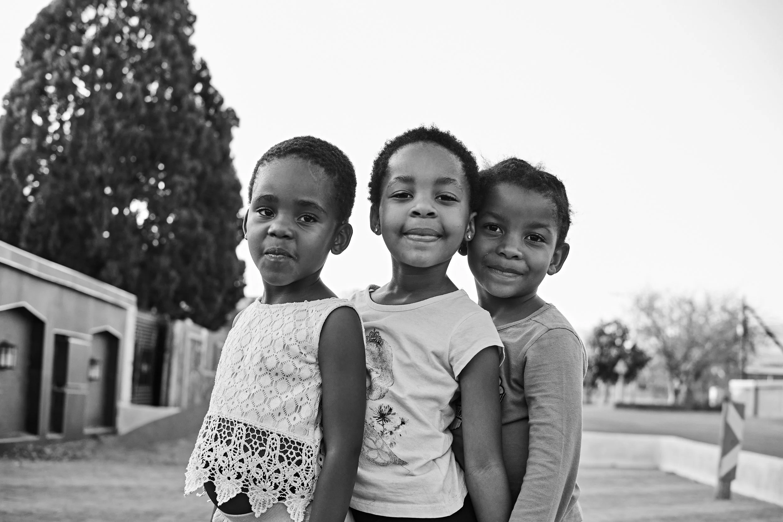 Three smiling children standing outdoors, black and white photo.