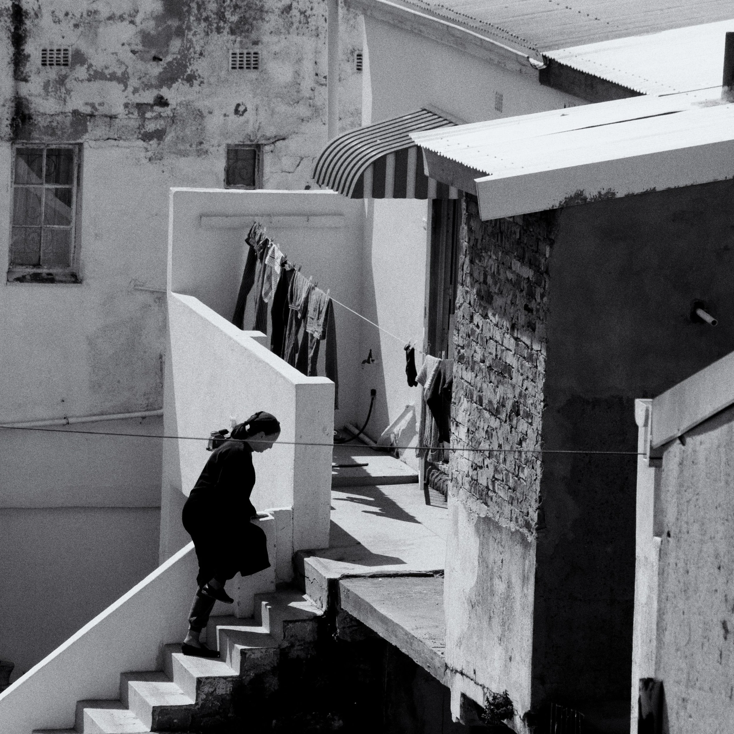 Black and white photo of a person ascending stairs next to a building, with a line of laundry hanging above.
