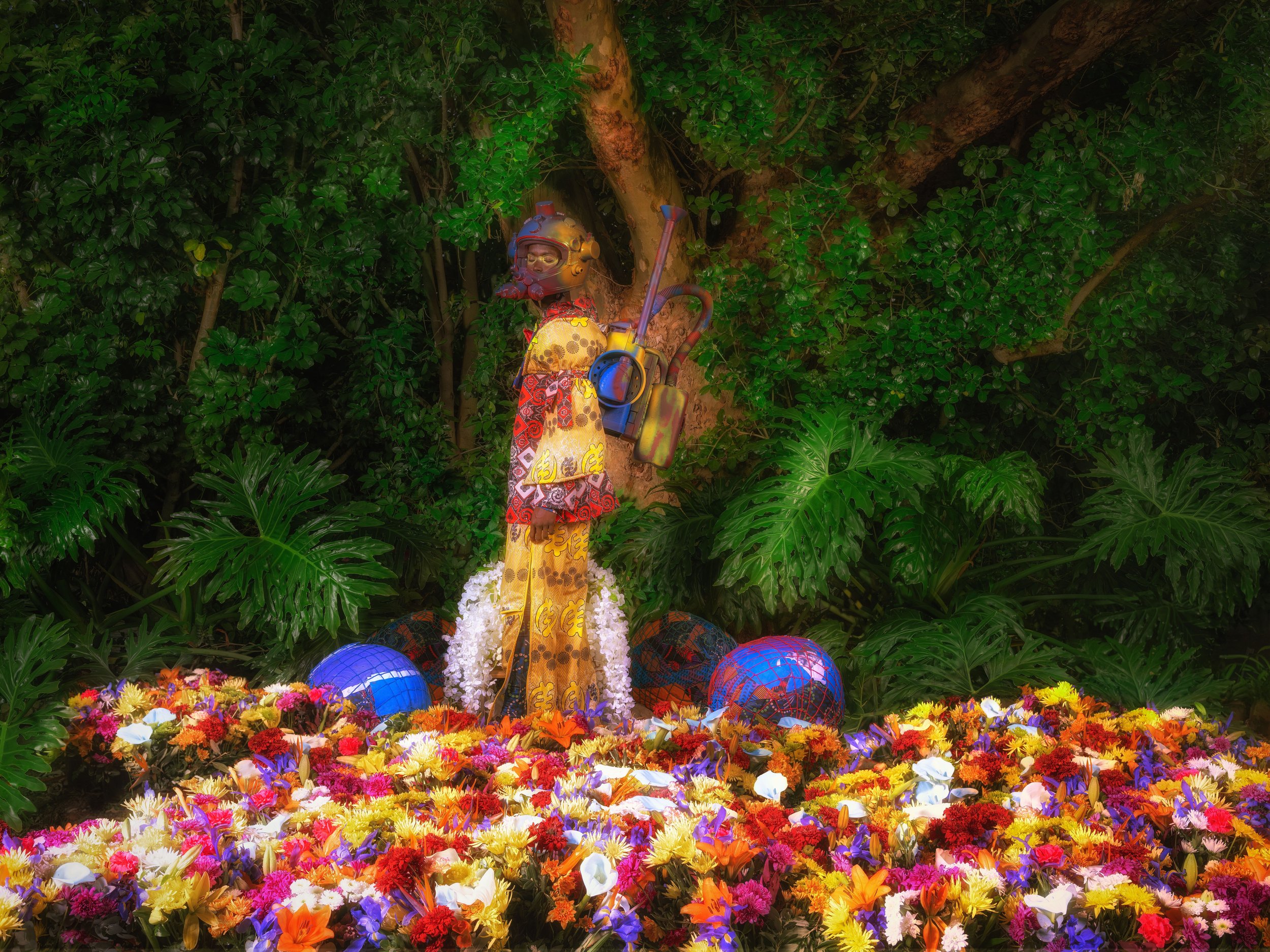 Colorful floral arrangement with mannequin in ceremonial attire and helmet, jungle backdrop.