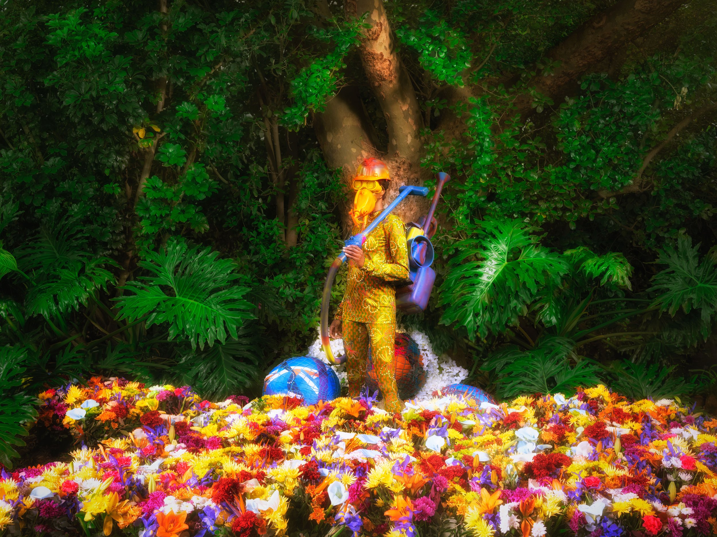 Person in colorful costume amidst vibrant flowers and green foliage.