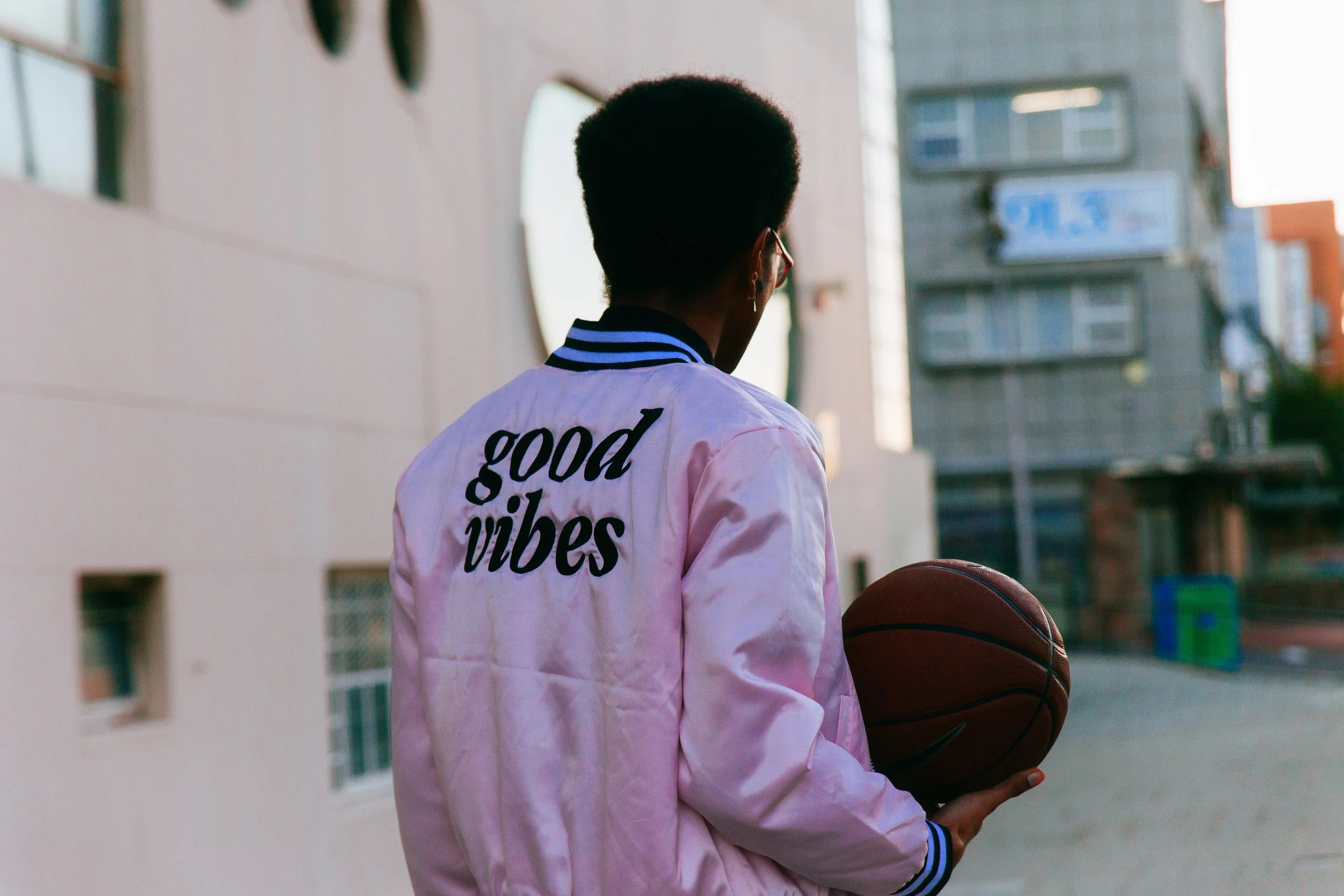 Person wearing a jacket with the words 'good vibes' holding a basketball in an urban setting.