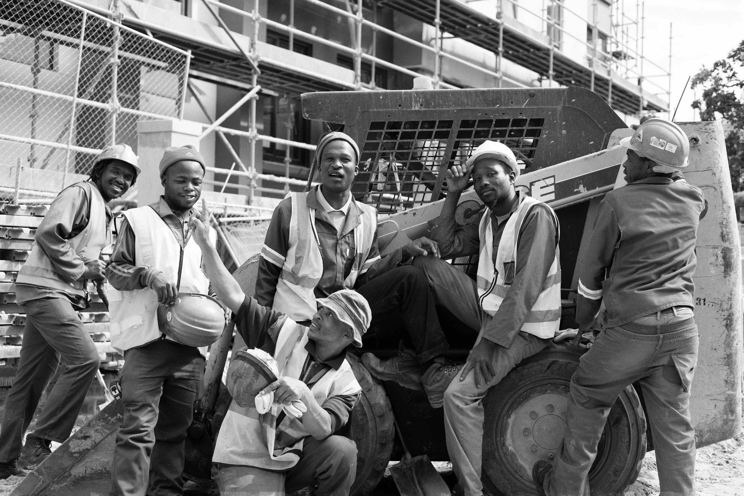Group of construction workers in vests and helmets at a construction site with scaffolding in the background.