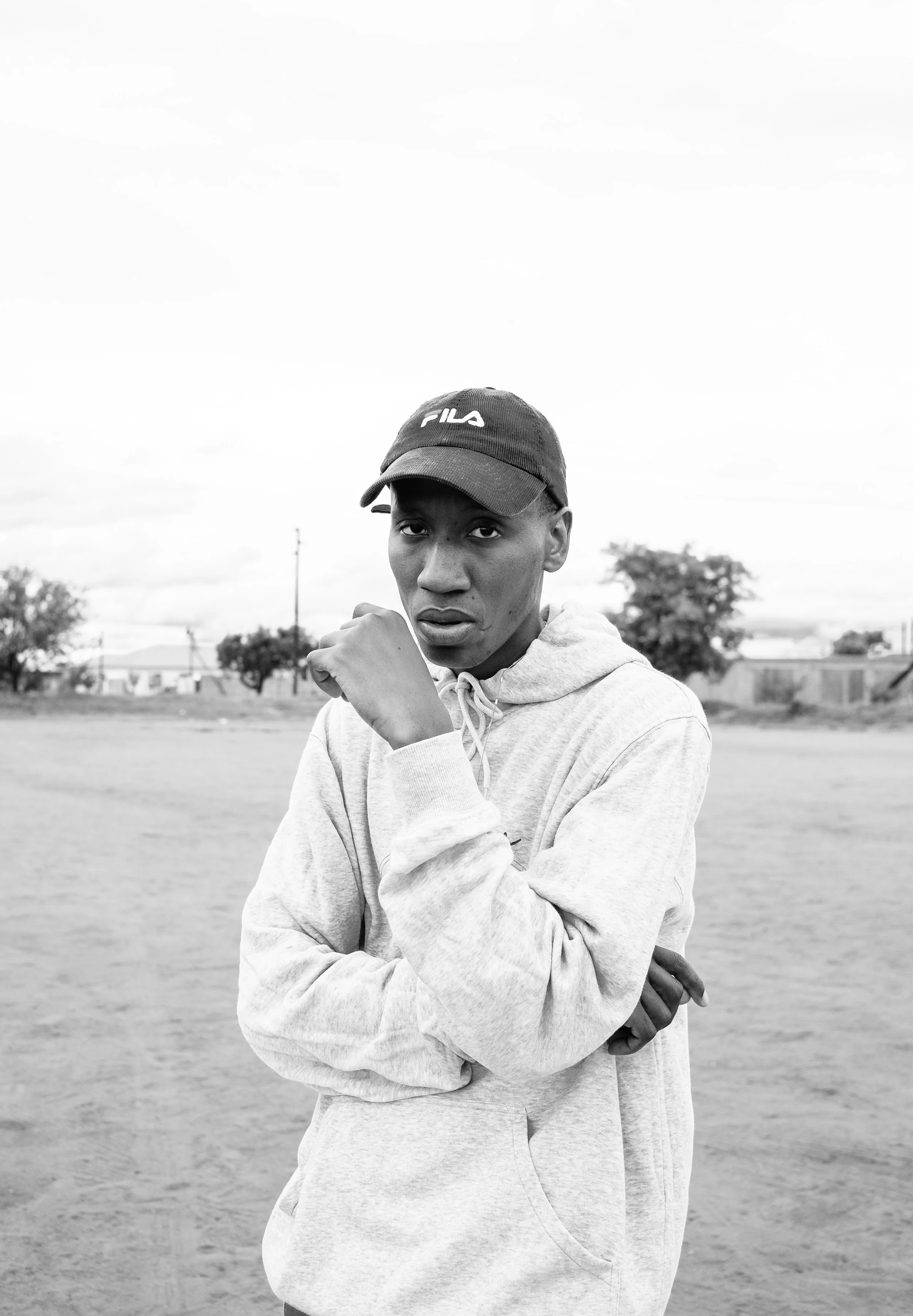 Black and white photo of person wearing a hoodie and cap in an outdoor setting.