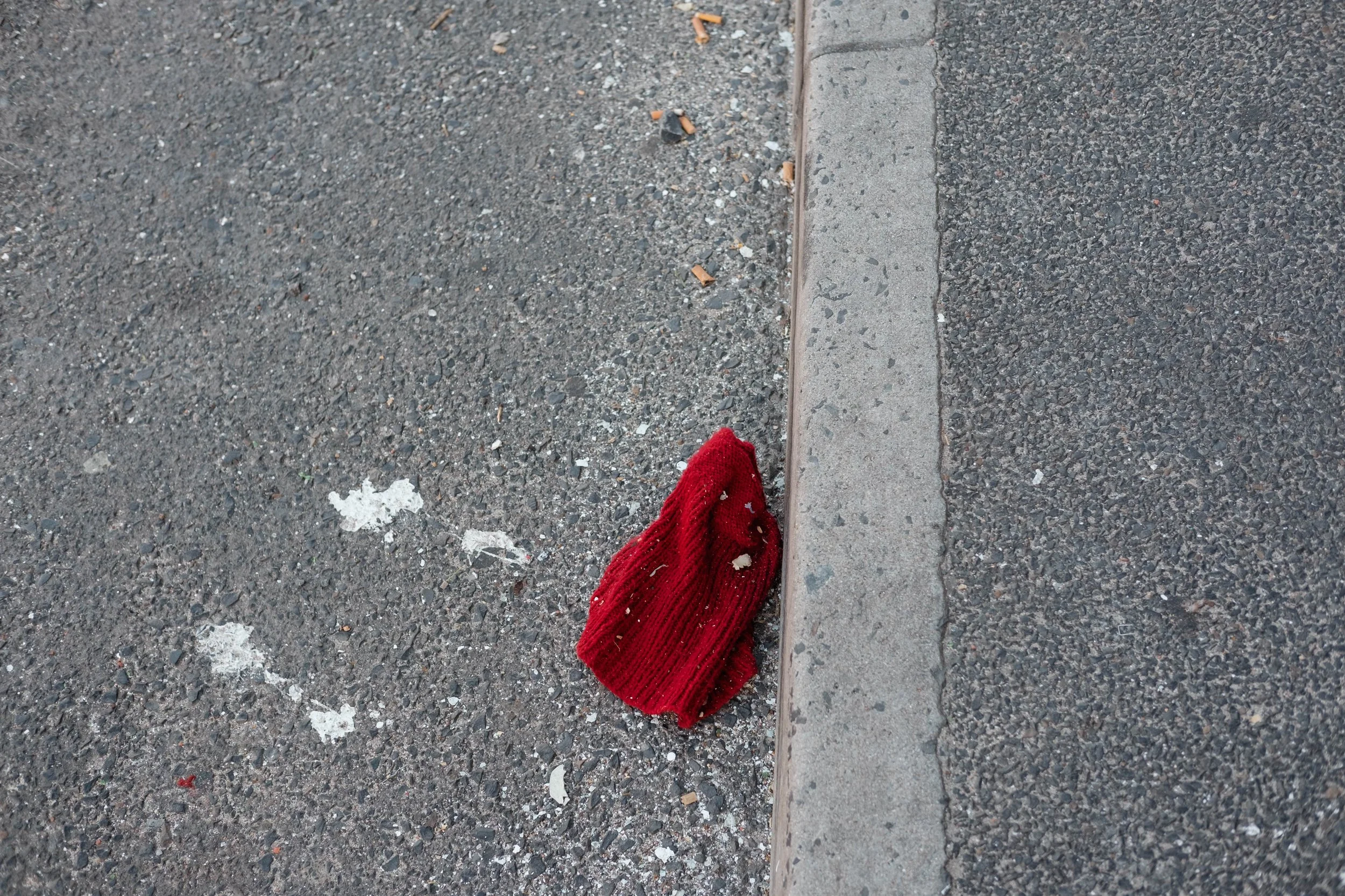 Red knitted hat on a concrete sidewalk near the street curb.