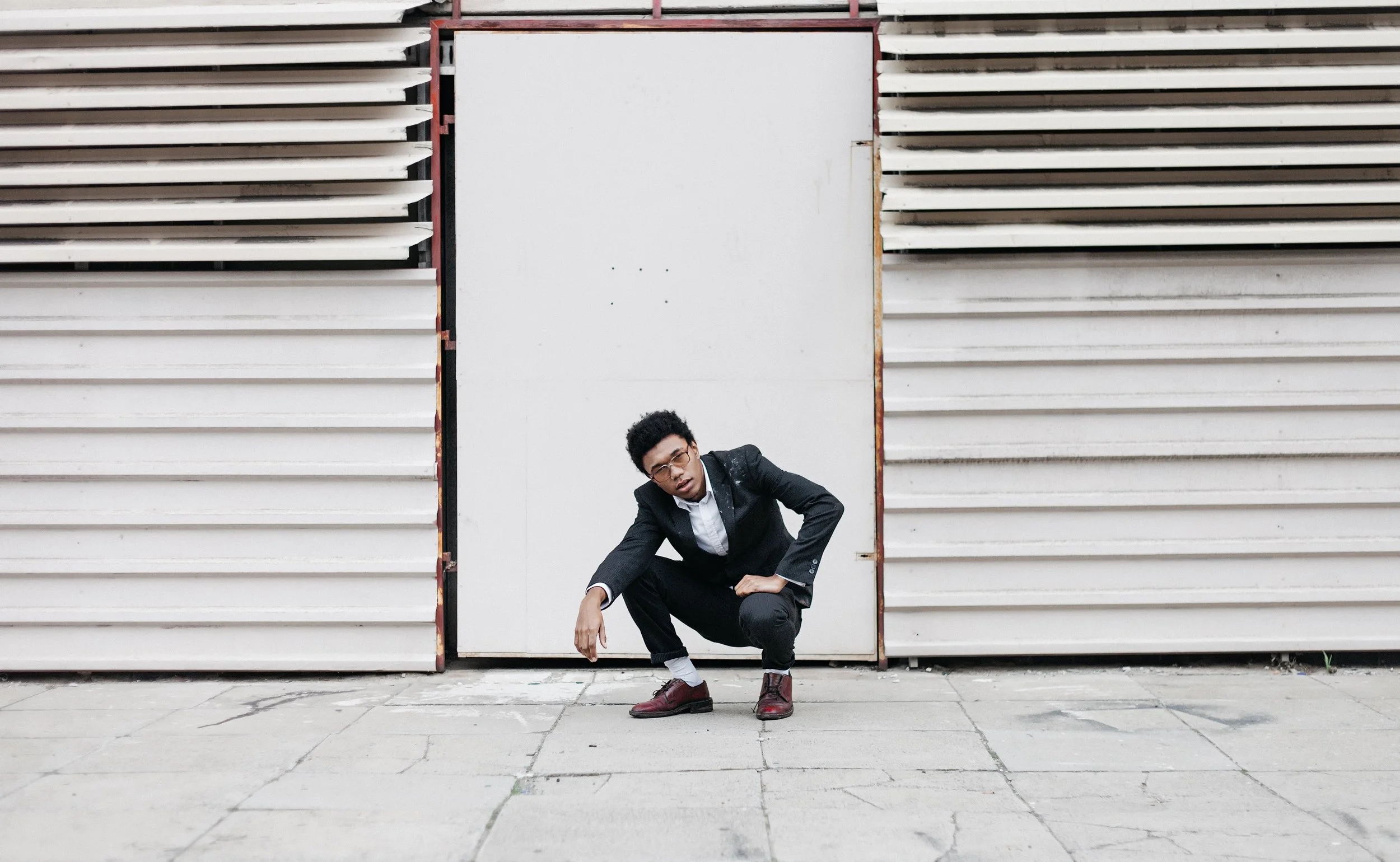 Man in black suit crouching in front of industrial building facade