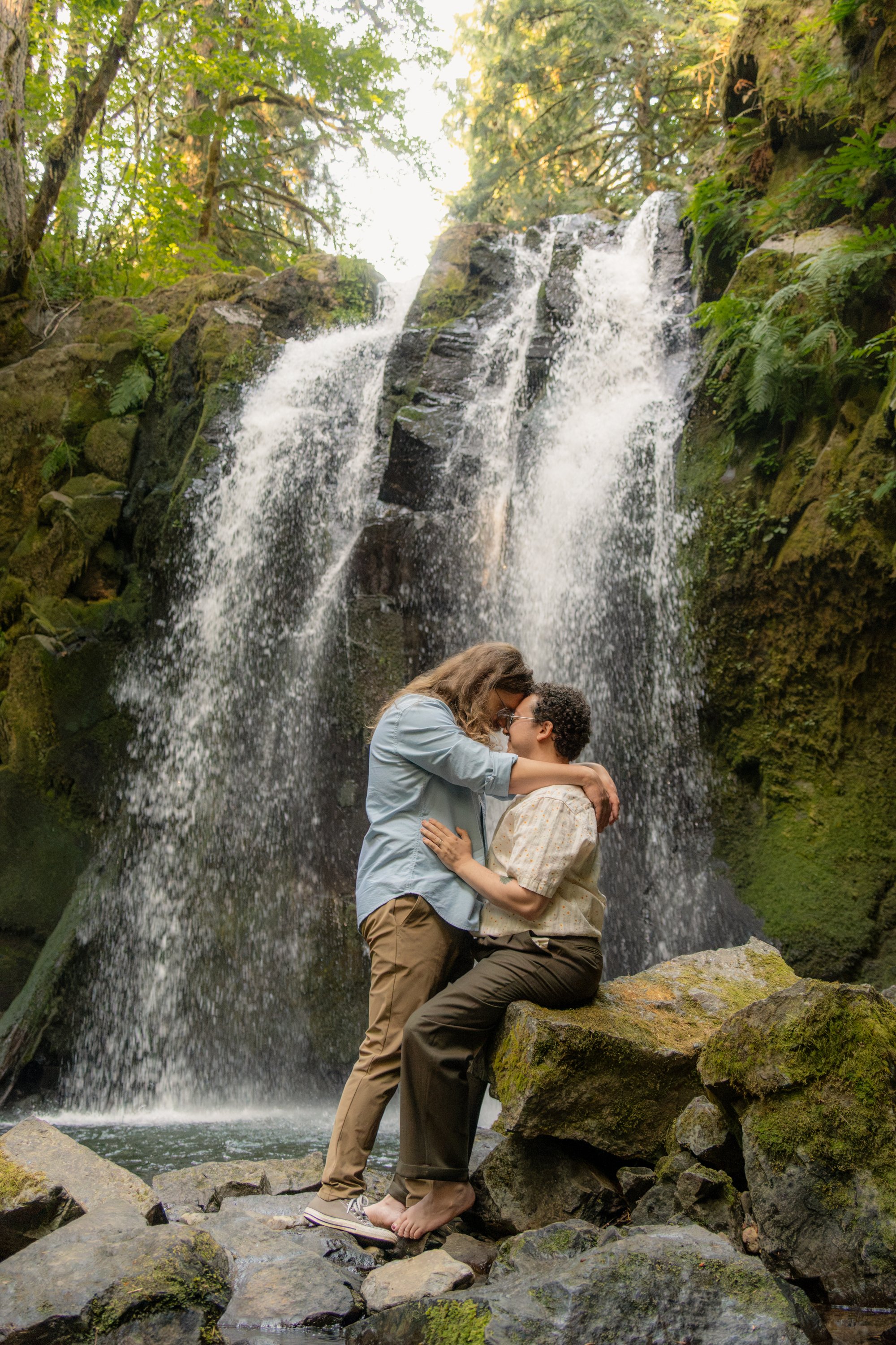 A couple embracing under a waterfall in a lush forest.