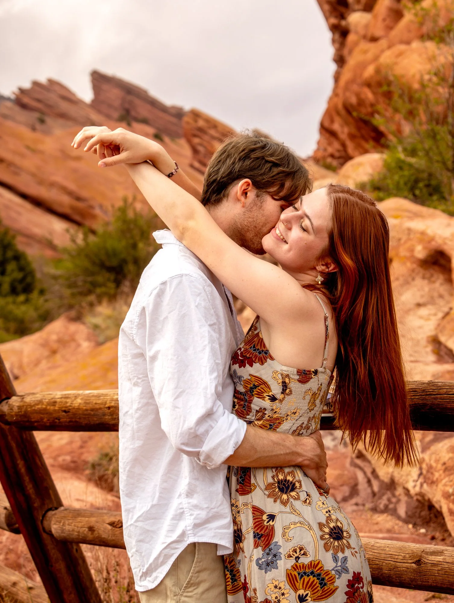 A couple sharing a romantic kiss outdoors with red rock formations in the background.