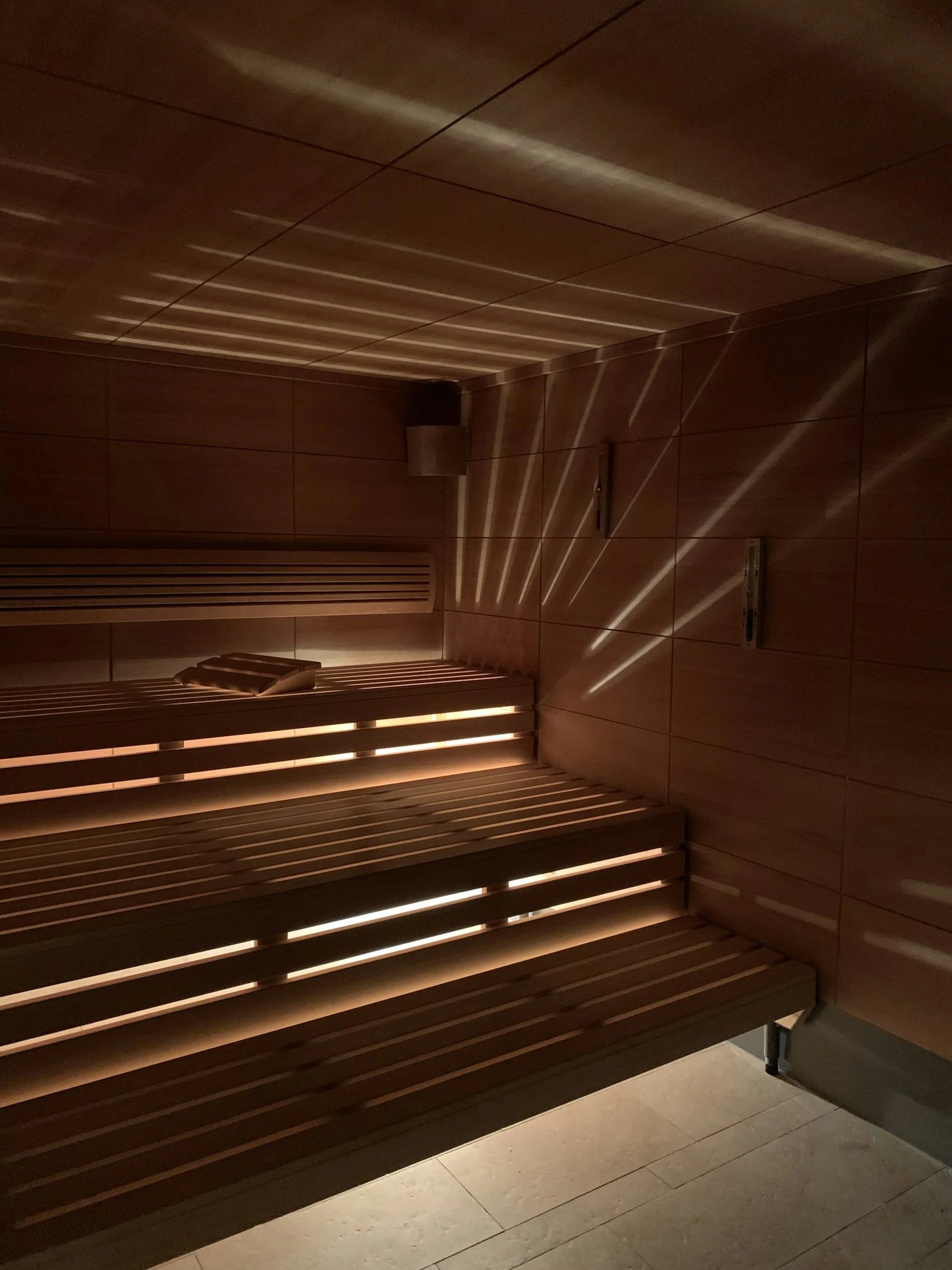 Indoor wooden sauna with benches and subdued lighting, with angled wooden slats on the walls and ceiling.