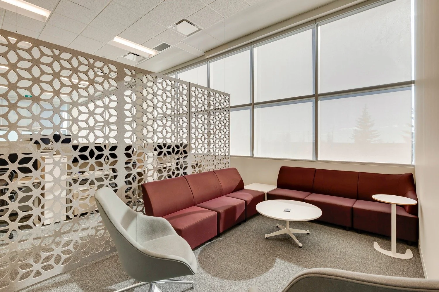 A beautifully designed, brightly lit commercial office space featuring bright red couches and a contemporary room divider.