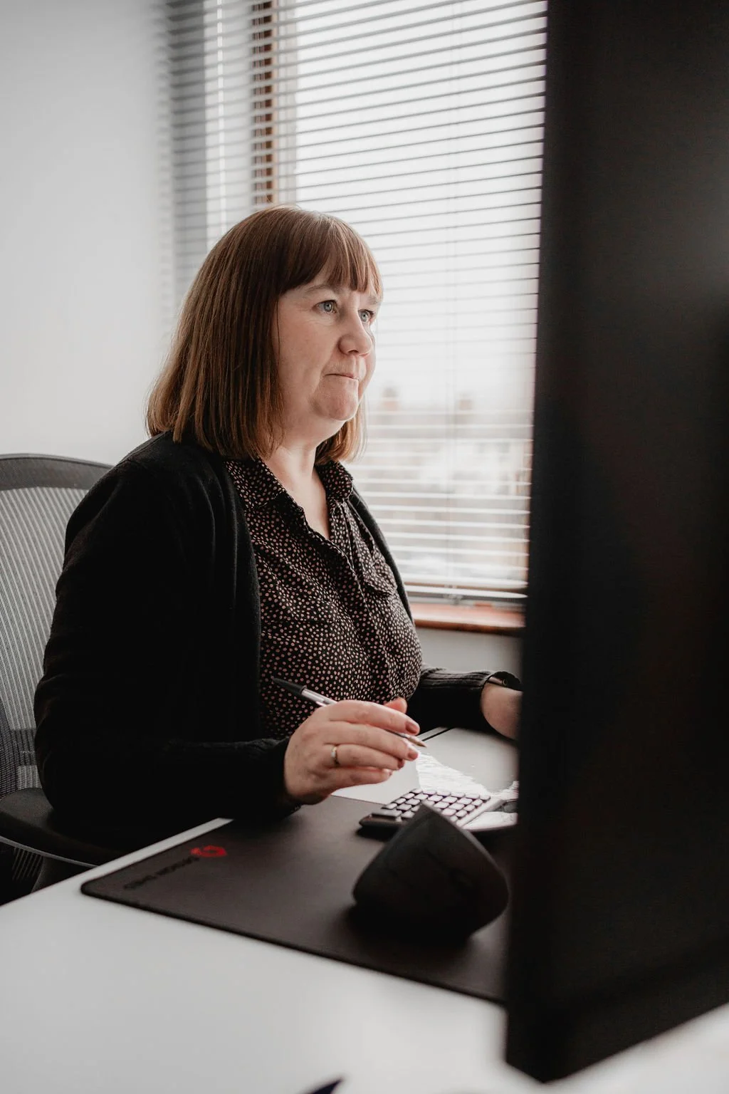 Image of founder Rachel Robinson, looking at computer screen whilst sat at a desk with pen in one hand and mouse in the other.