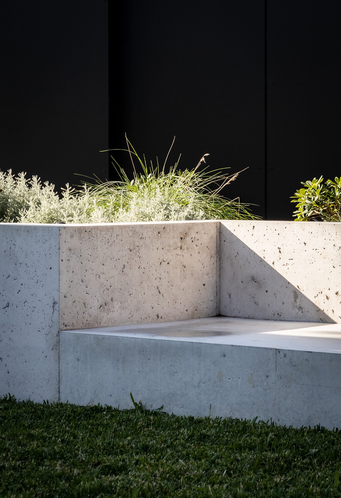 Modern concrete bench with plants and grass in a landscaped garden setting, featuring a dark backdrop.