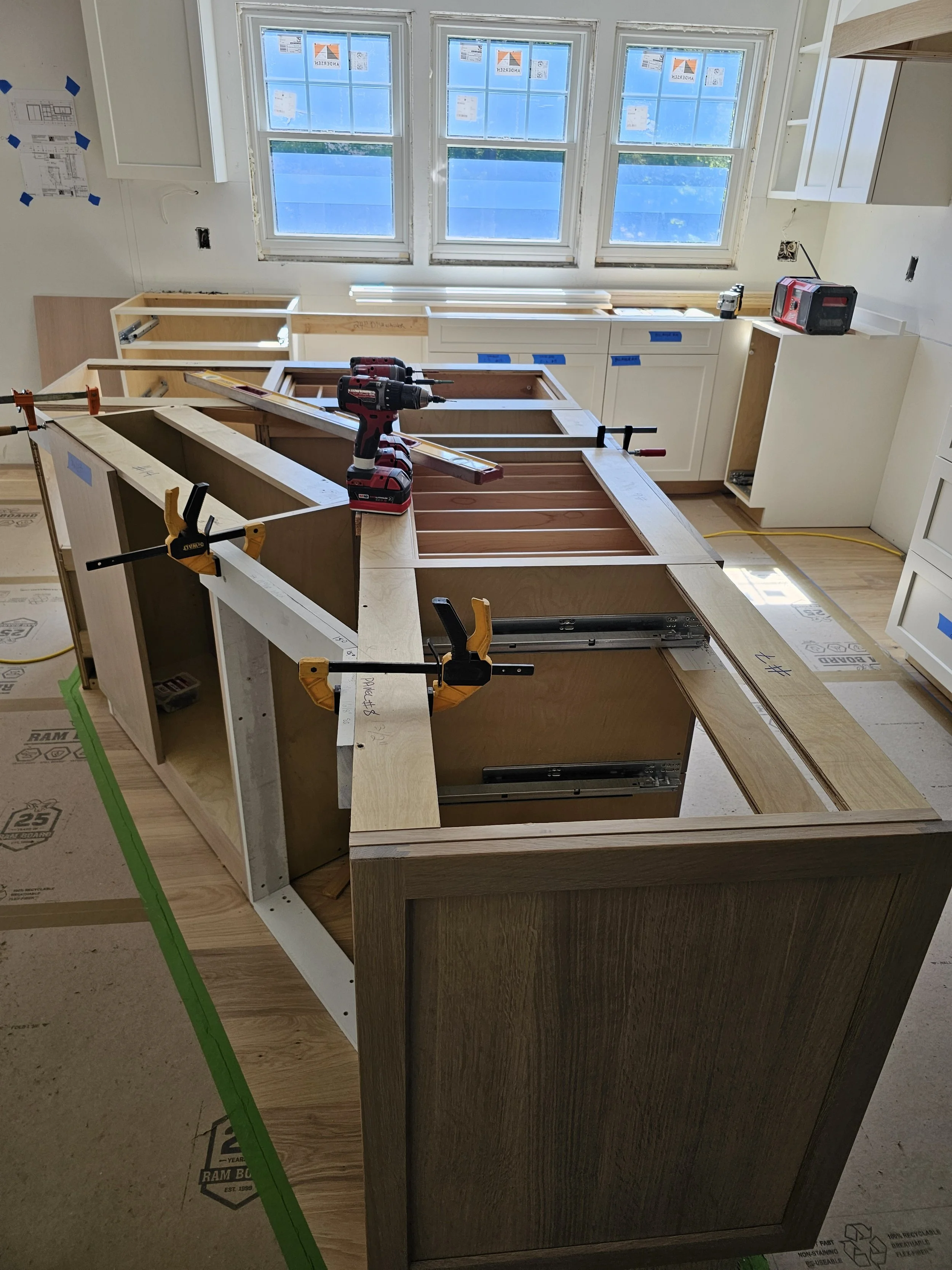Kitchen under construction with cabinets, tools, and construction materials visible.