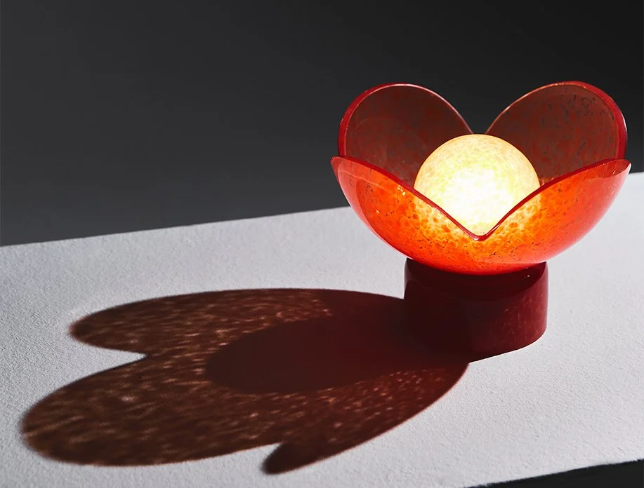 The red flower-shaped glass Lucky Akebia Table Lamp by Anna & Sergii Baierzdorf shining with soft light in a dark room.
