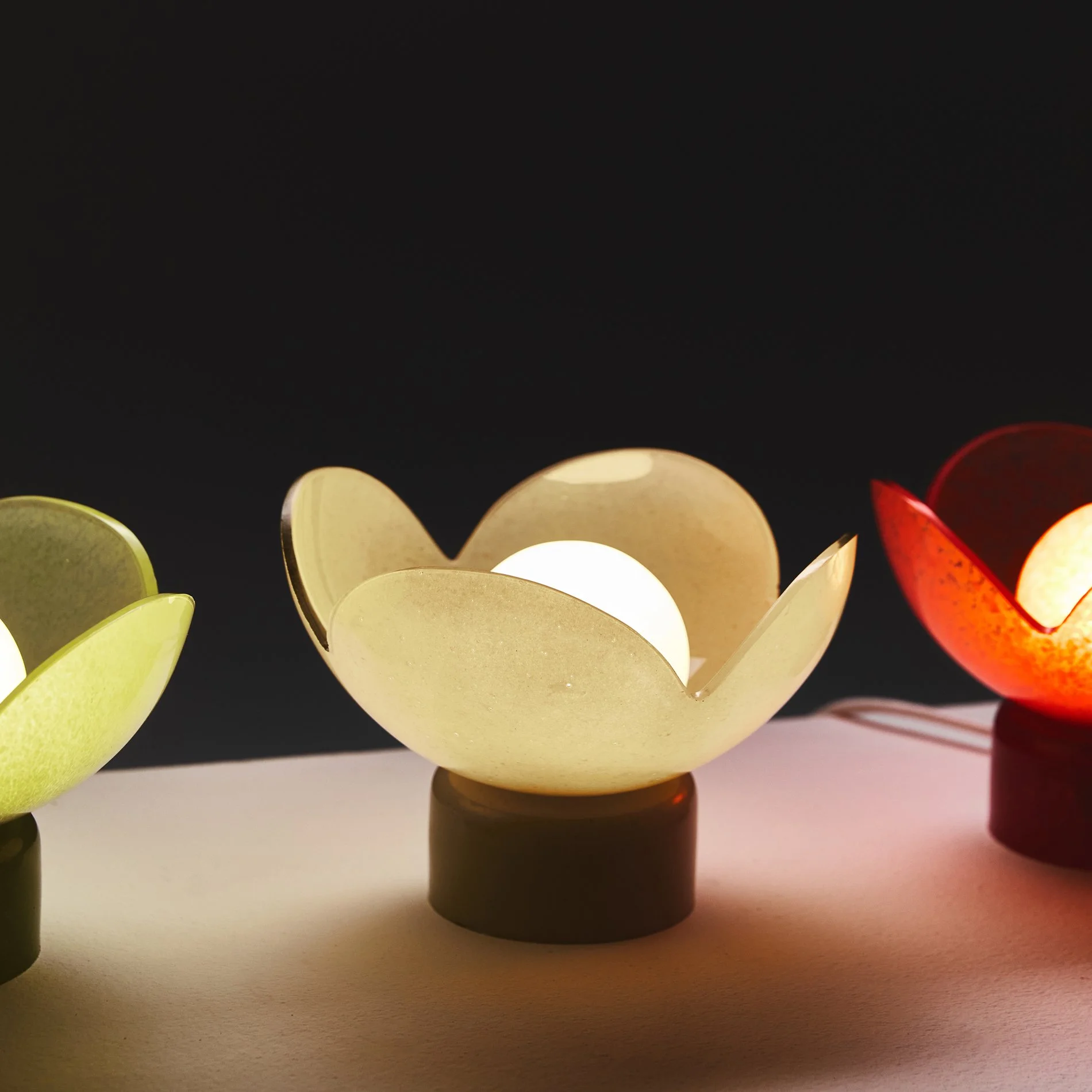 Flower-shaped Lucky Akebia glass lamps lit up on a dark background