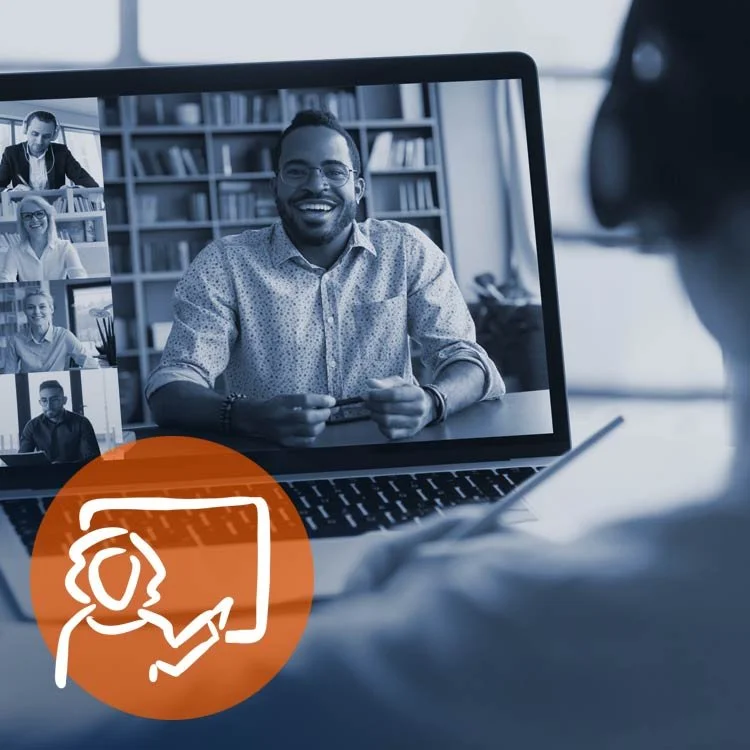 People participating in a virtual meeting on a laptop, with a woman in the foreground taking notes and a smiling man on the screen in a library setting.