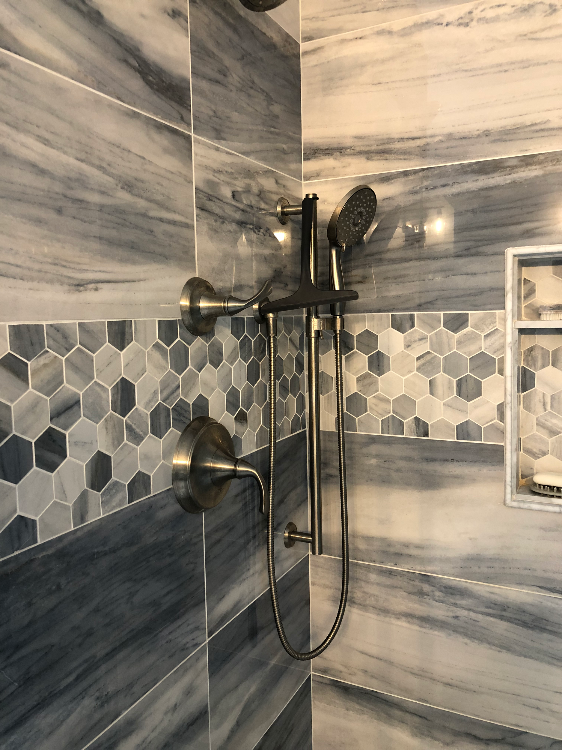 Bathroom with marble and hexagon tile design, featuring bathtub fixtures, including a hand shower and faucet, set against a gray and white color scheme.