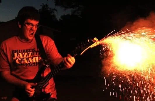Person playing guitar outdoors at night while igniting and holding a sparkler.