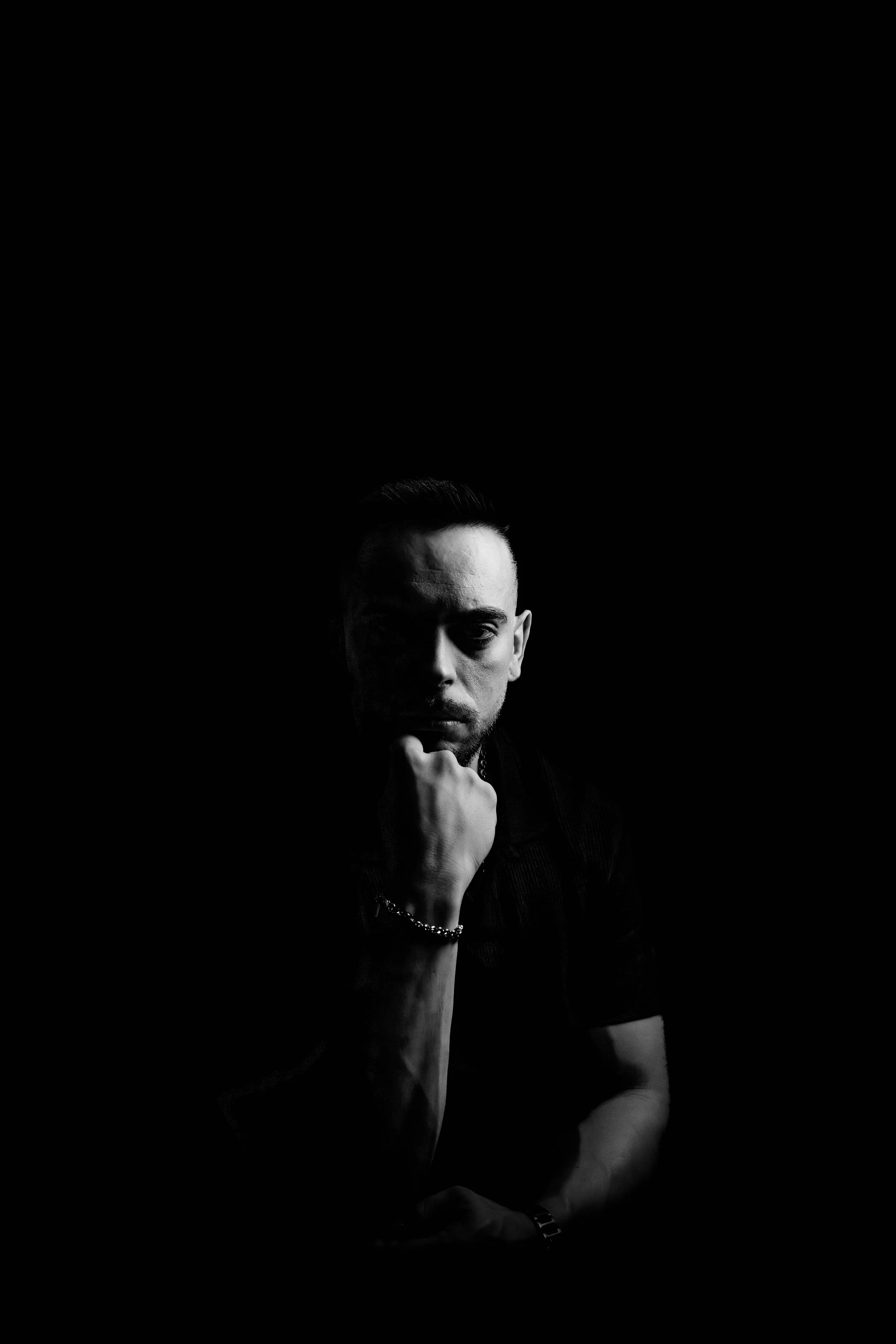 Fotografía artística en estilo low-key, donde el juego entre luz y sombra destaca la mirada y la estructura facial del sujeto. El blanco y negro aporta una estética atemporal y poderosa, ideal para presentaciones visuales y branding personal. Trabajo