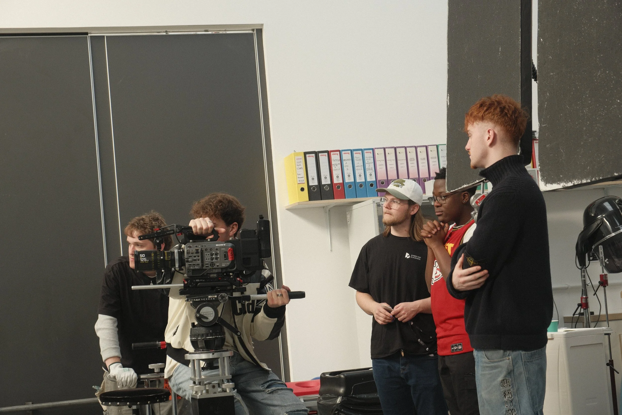 Group of young people working on a film project in a classroom, with a camera and filming equipment.