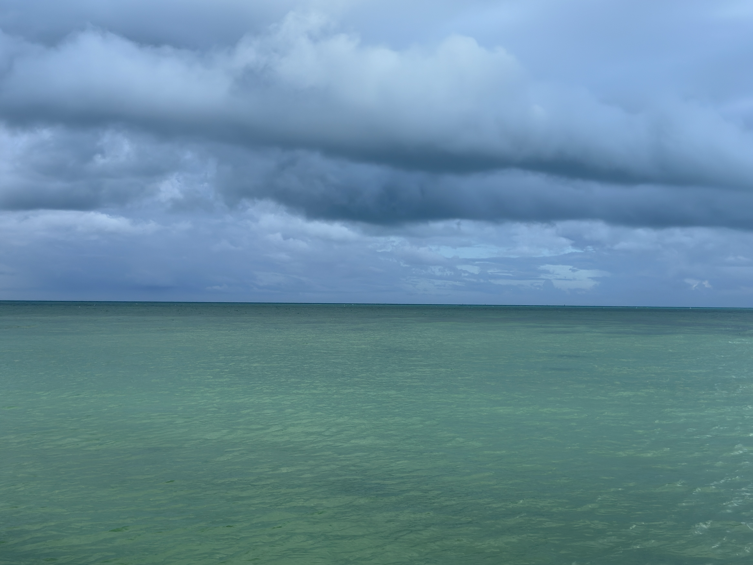 Cloudy sky over a calm ocean with greenish-blue water.