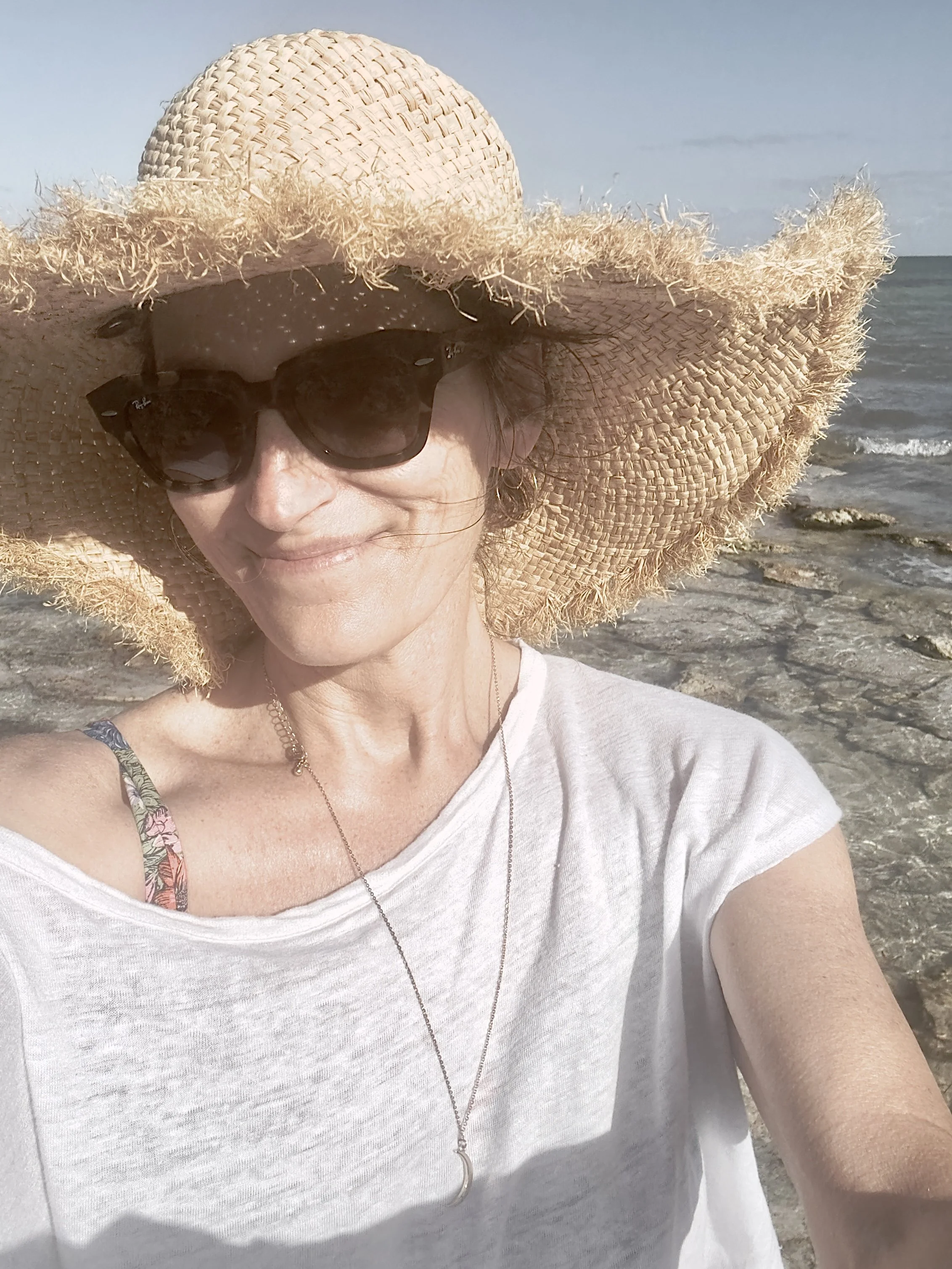 Person wearing a straw hat and sunglasses at the beach.