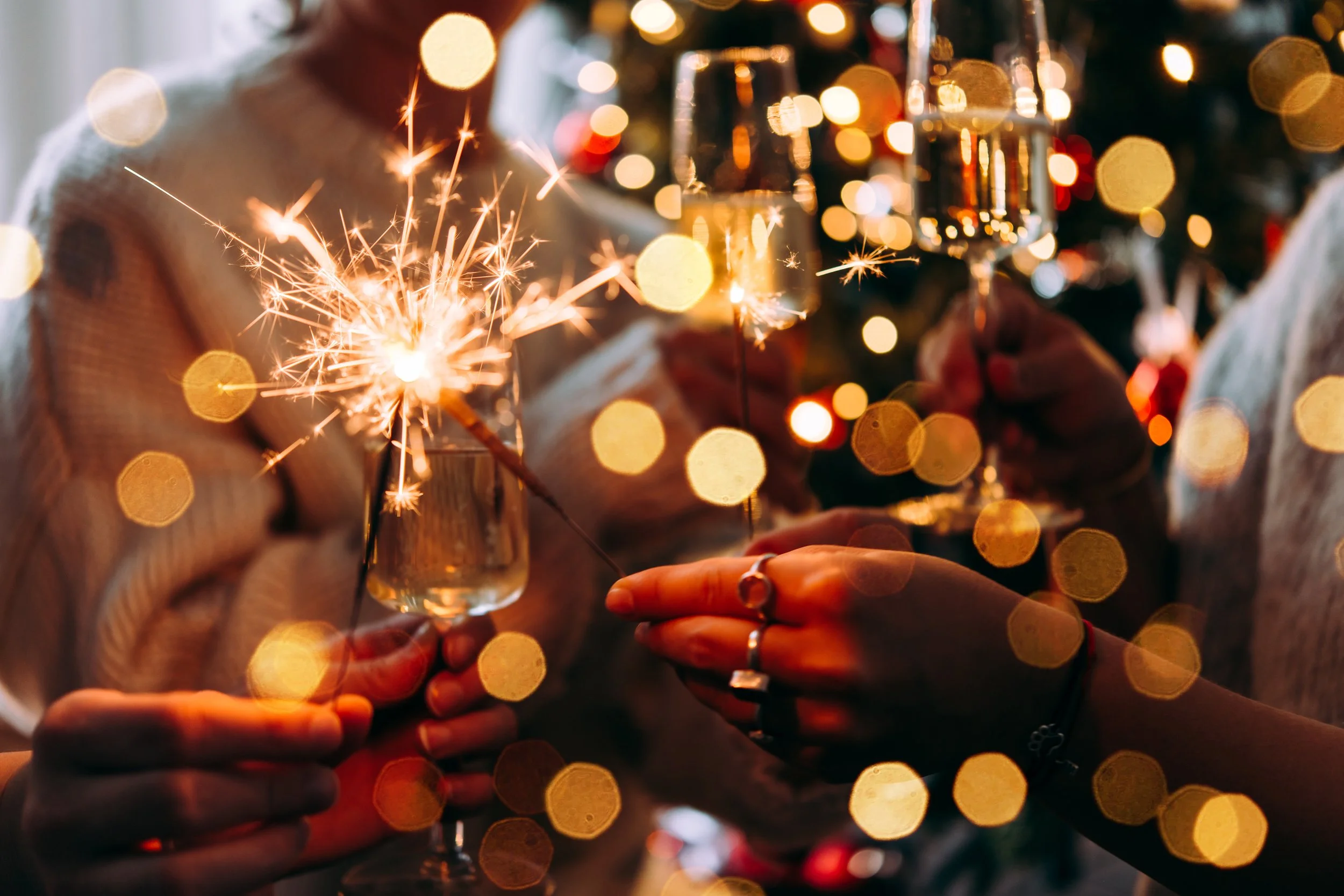 People holding sparklers and glasses of champagne at a festive celebration with blurred colorful lights in the background.