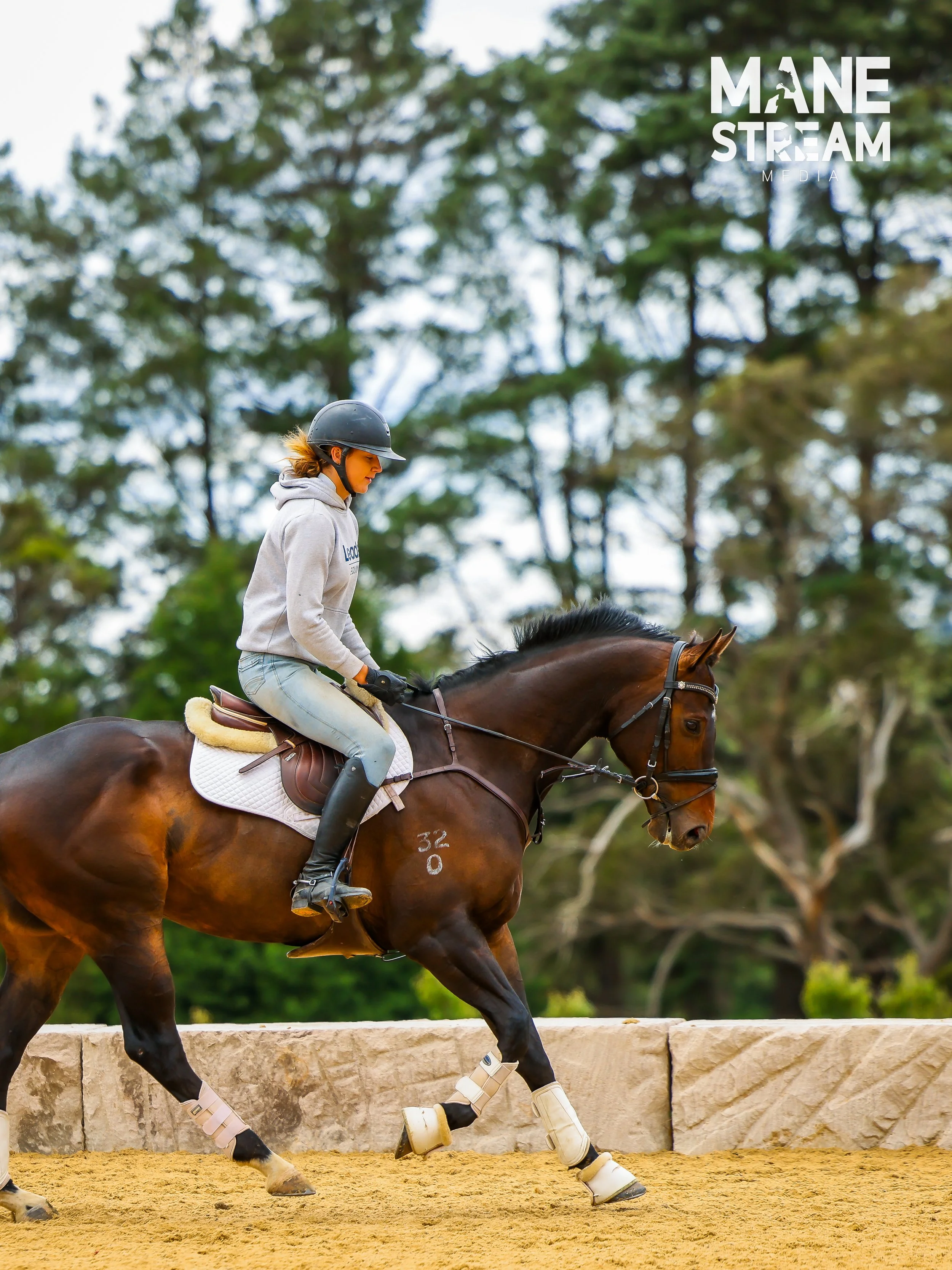 A woman with long blonde hair wearing a teal dress standing next to a grey horse in a forest.