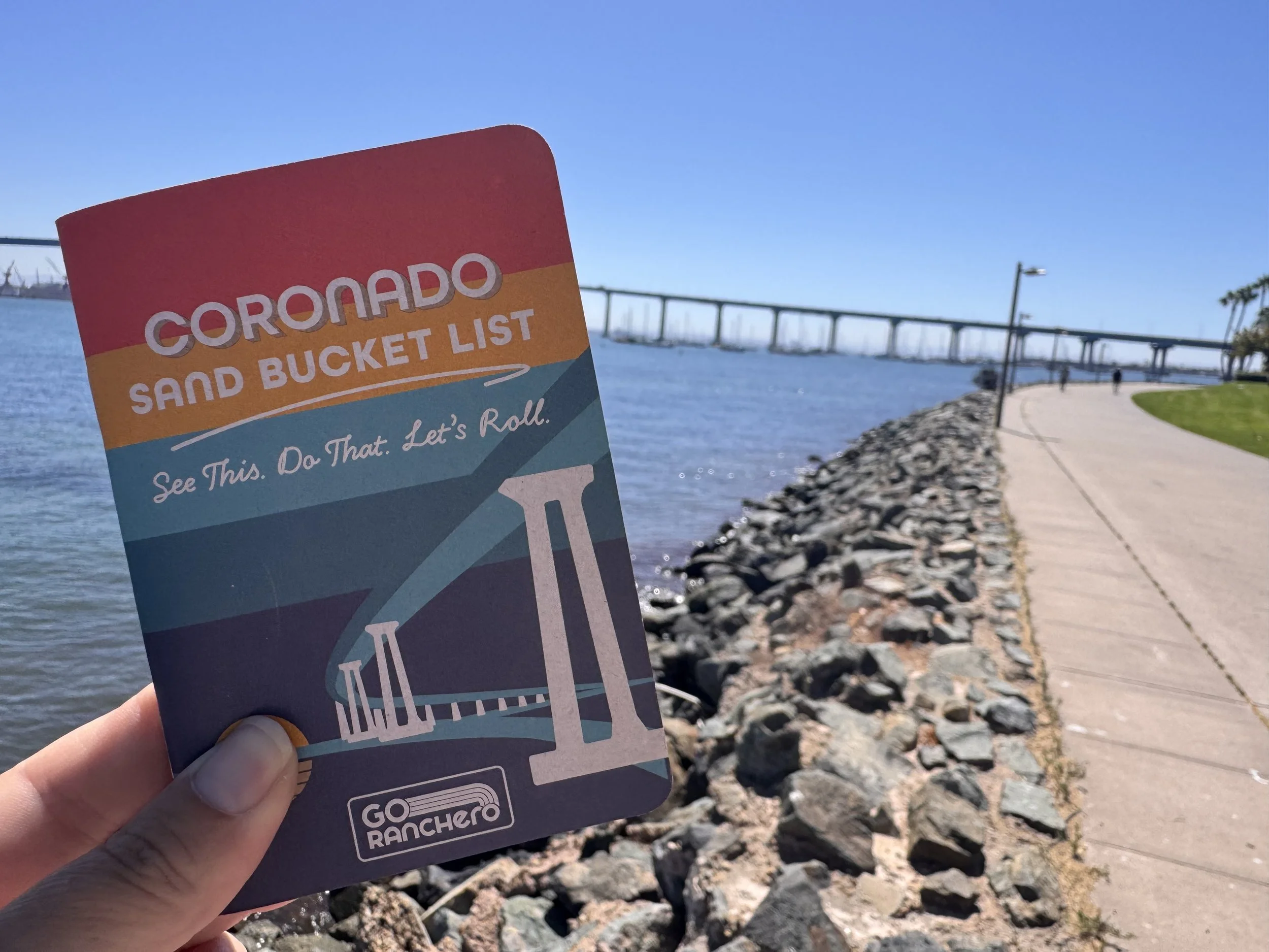 Coronado Sand Bucket List along the bayside walkway with the Coronado Bridge in the background
