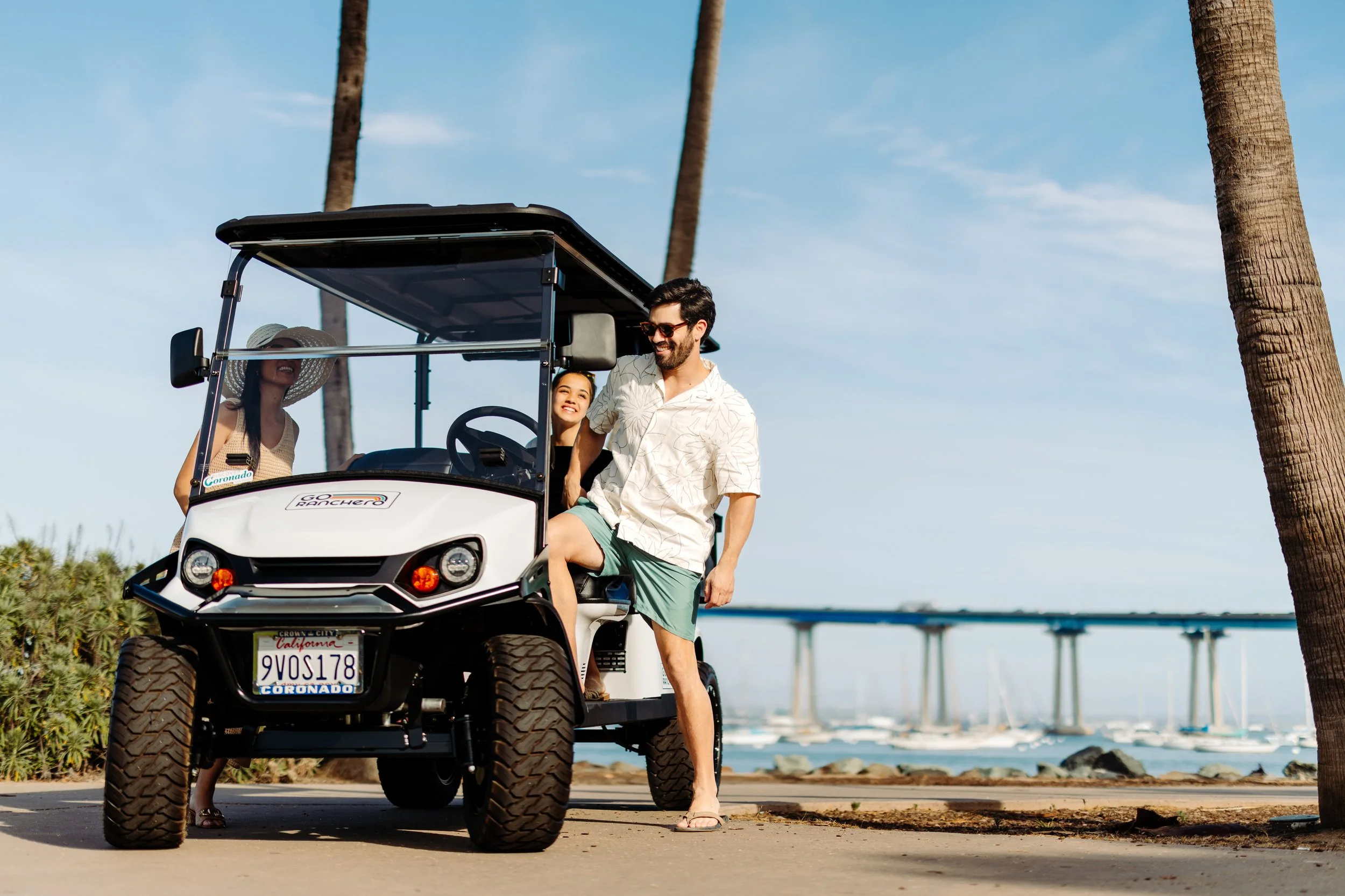 Go Ranchero golf cart with passengers along the Coronado waterfront with the Coronado Bridge in the background