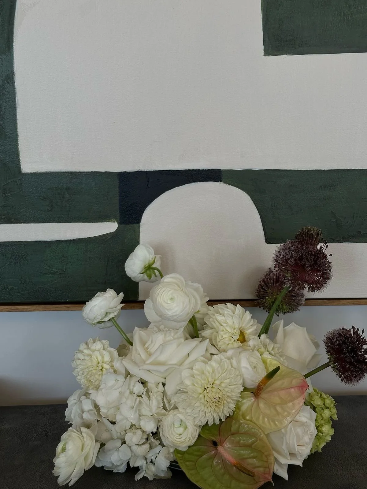 White and purple flower bouquet in front of a geometric abstract painting with white, green, and black shapes.