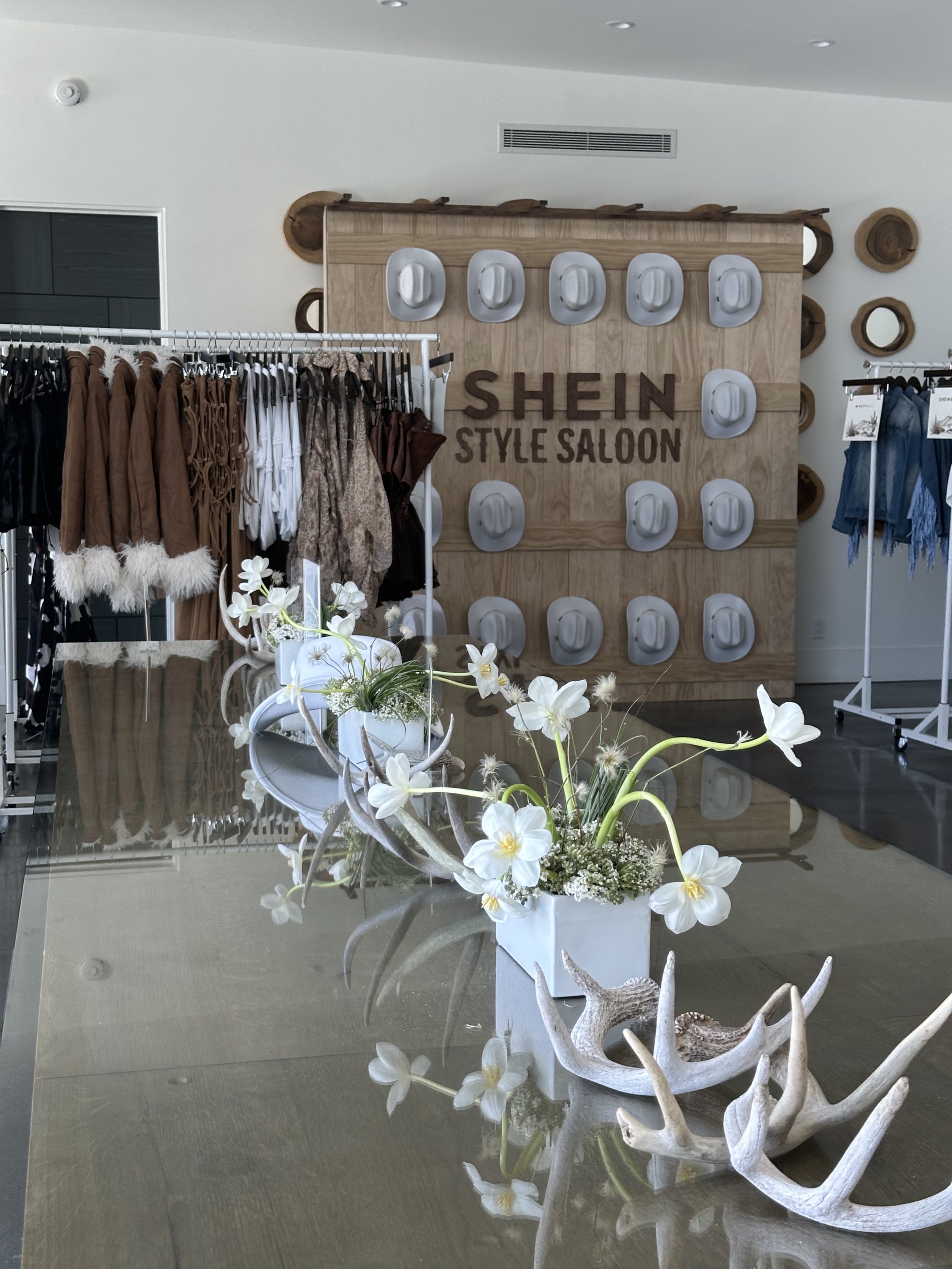 Interior of a clothing store named Shein Style Saloon with clothing racks and decorative antlers and flowers on a table.