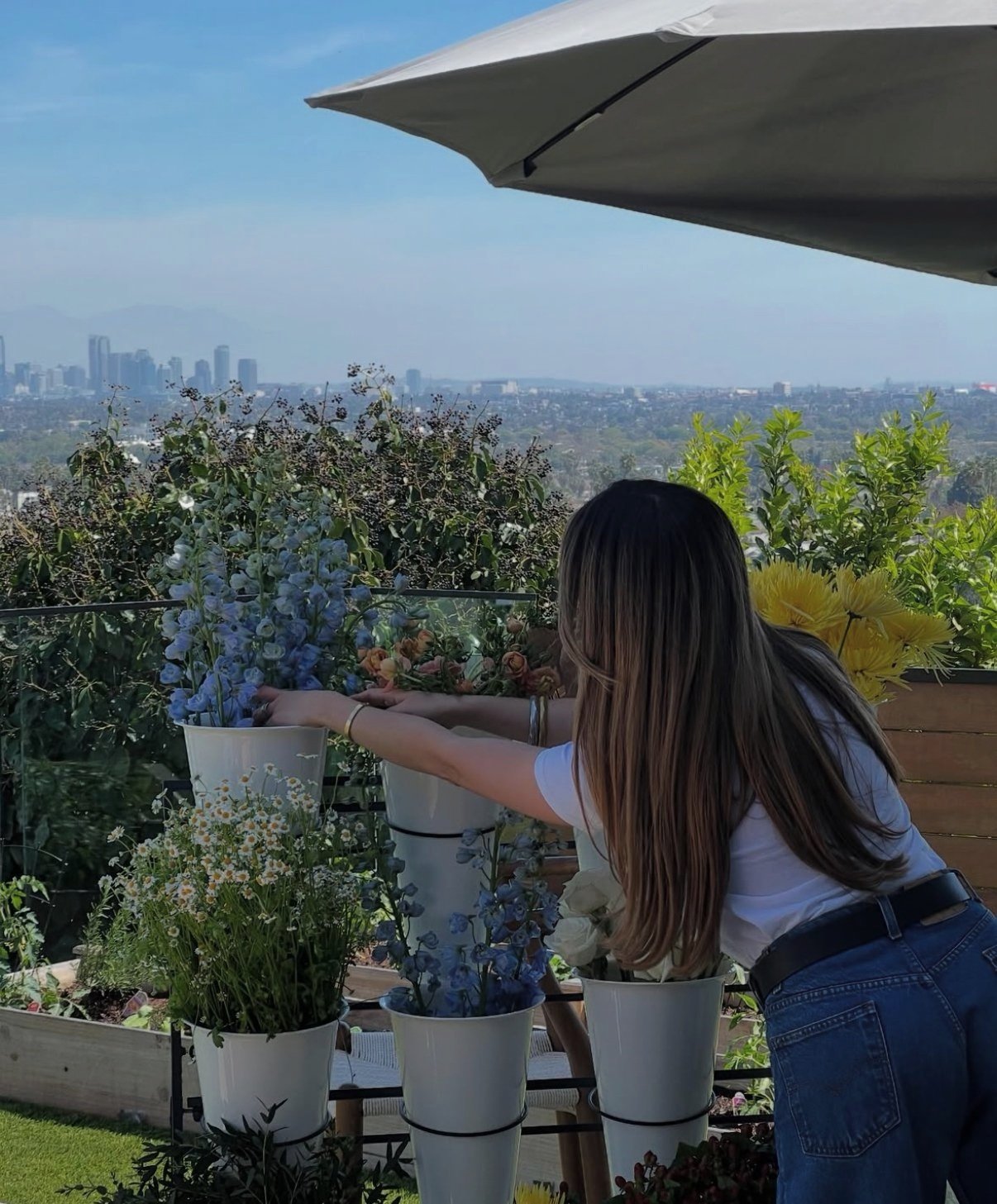 A woman arranging flowers on a rooftop garden with a city skyline in the background.