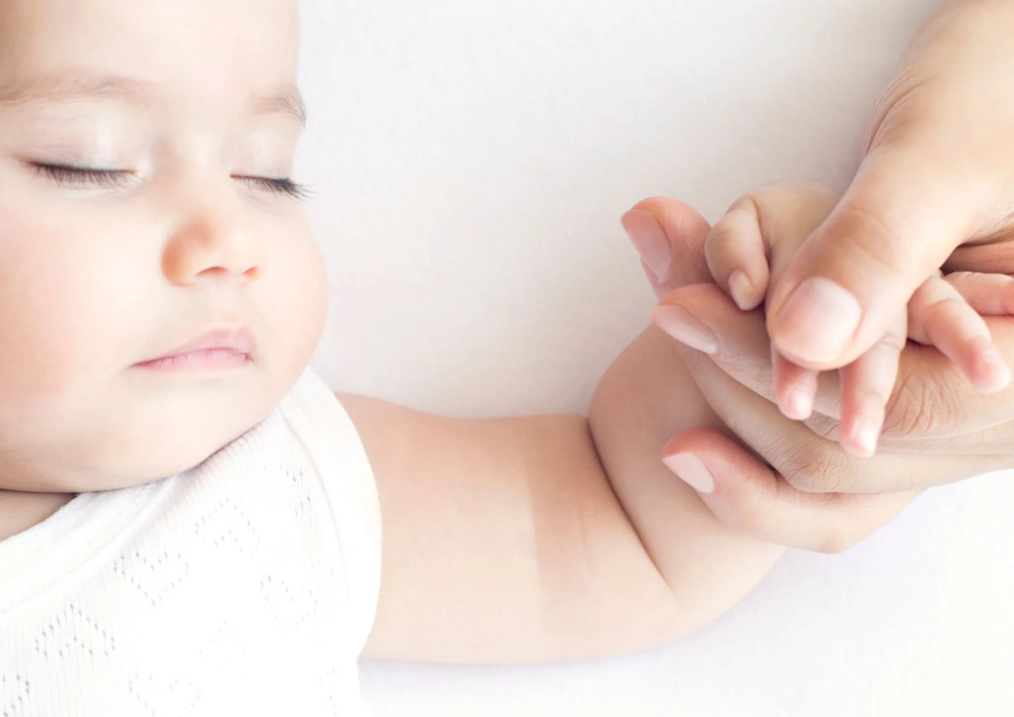 A young child with closed eyes and a calm expression receiving gentle assistance with finger placement for an activity, possibly finger painting or a medical exam, with soft lighting and a neutral background.