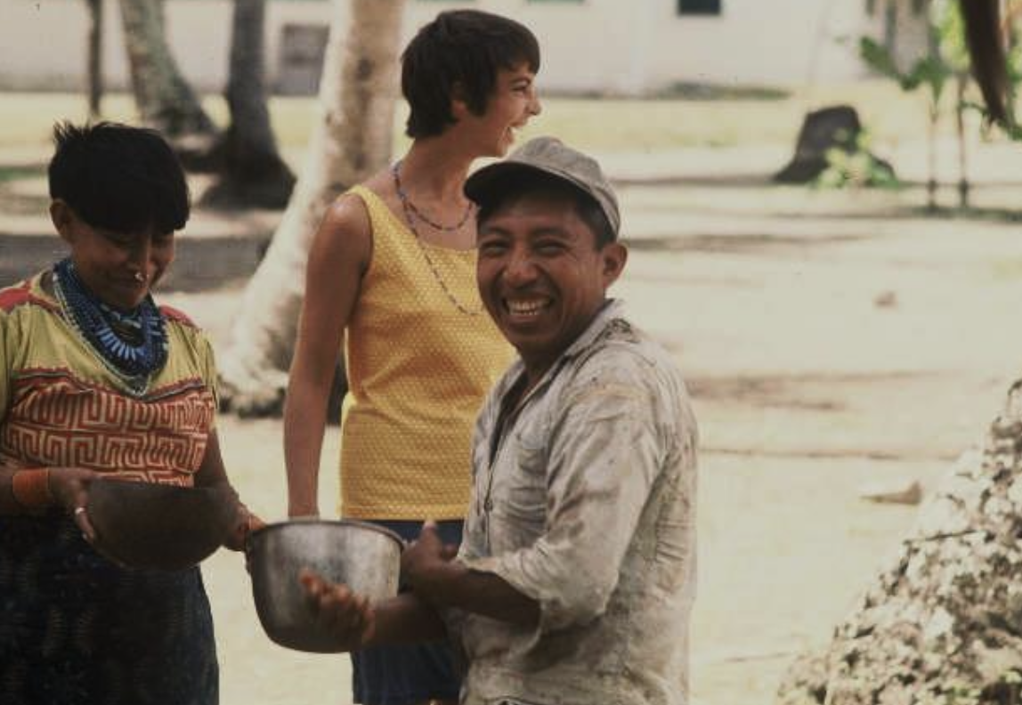 Three people outdoors smiling and holding bowls, with trees and a building in the background.