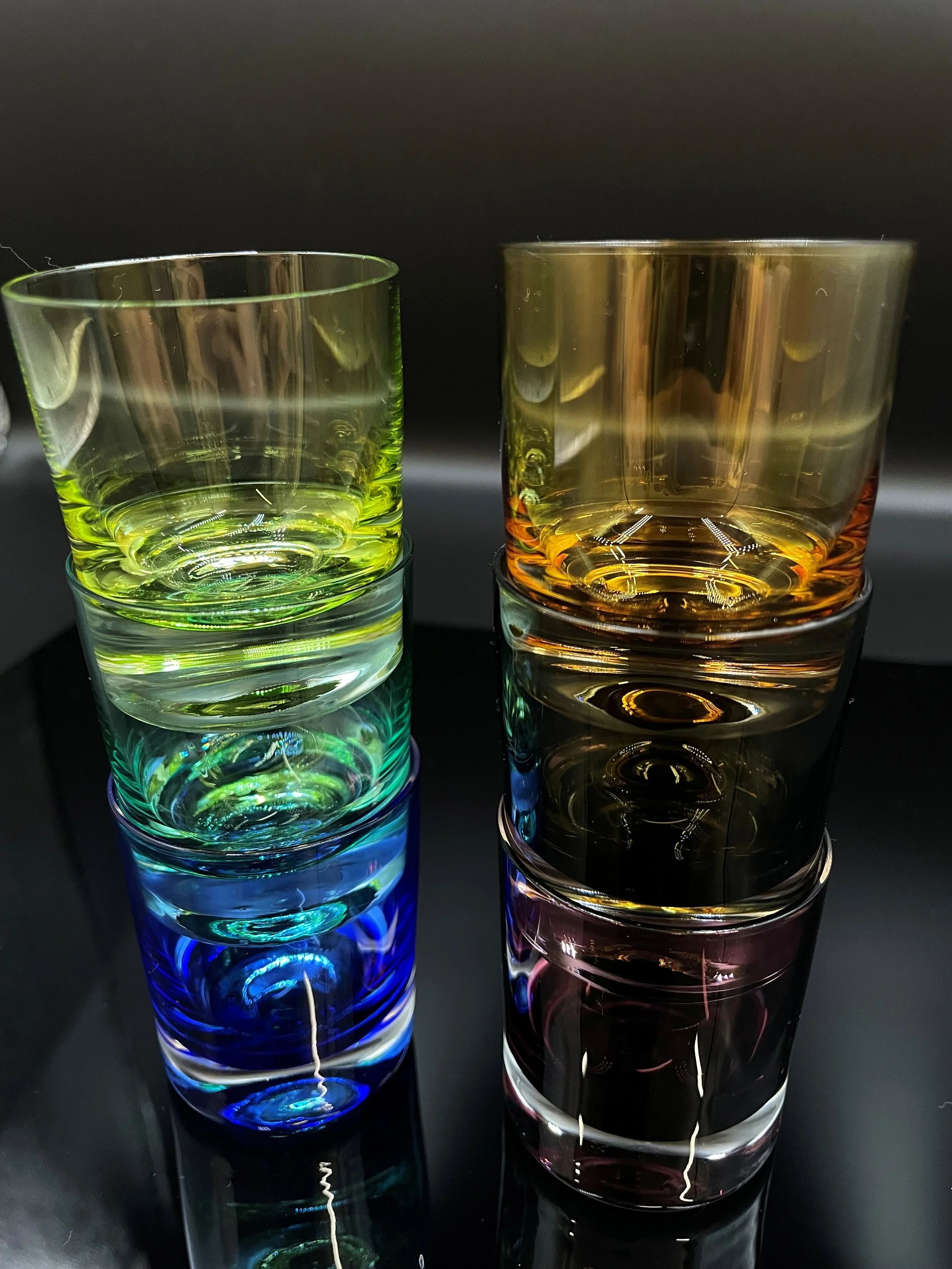Bunte Gläser mit Wasser in Schwarzlicht, die Farben leuchten und sich reflektieren.