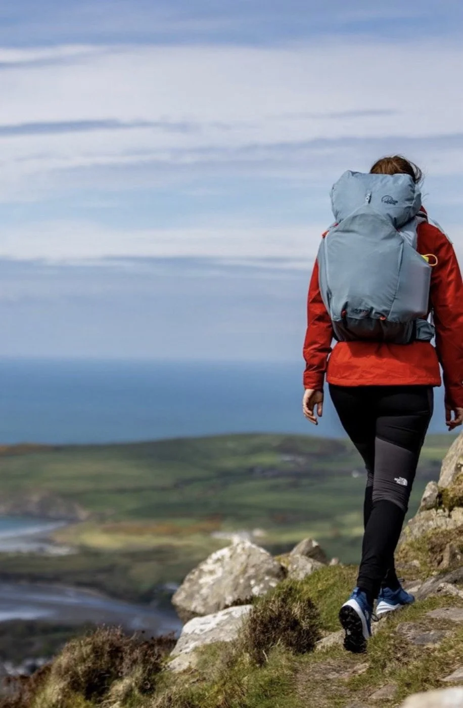 Emma walking away along a coastal ridge path with a large rucksack