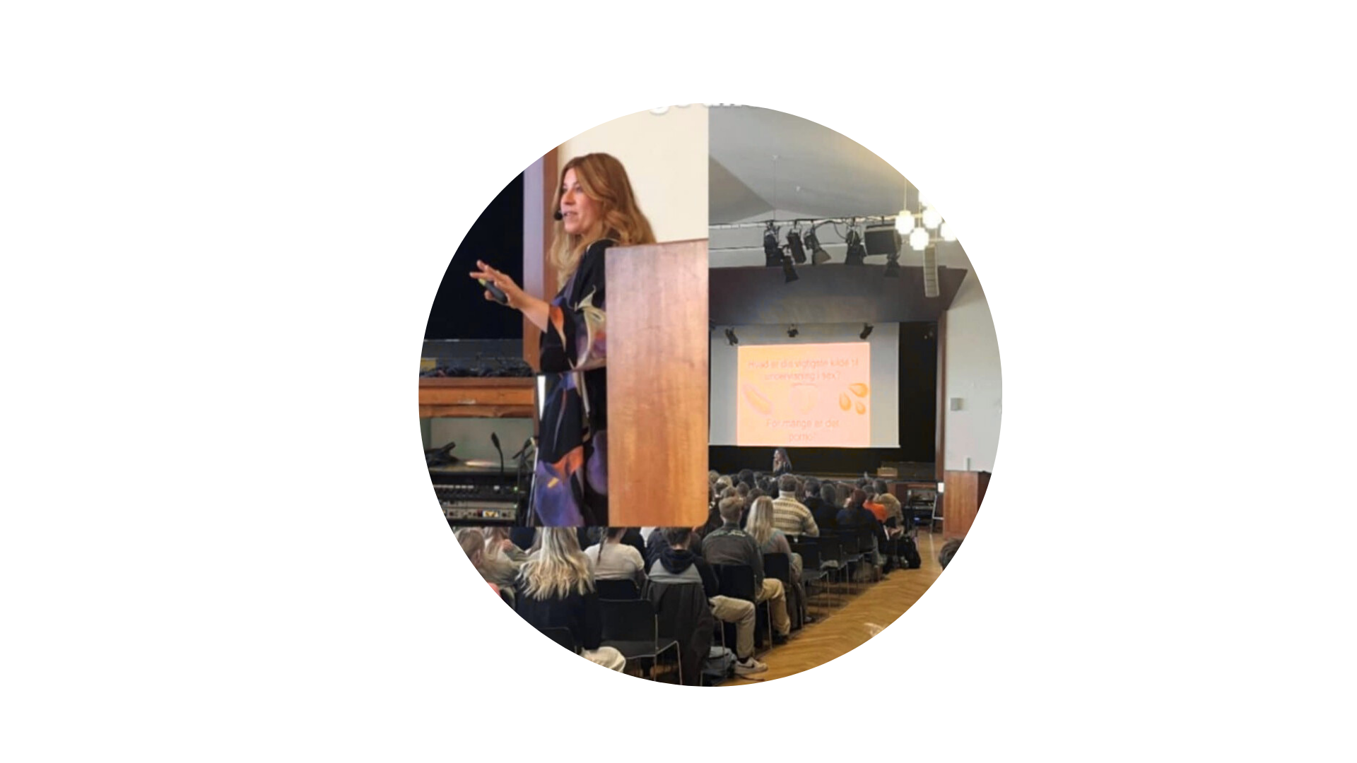 Indendørs konference med flere deltagere, der sidder omkring borde og ser på en skærm.