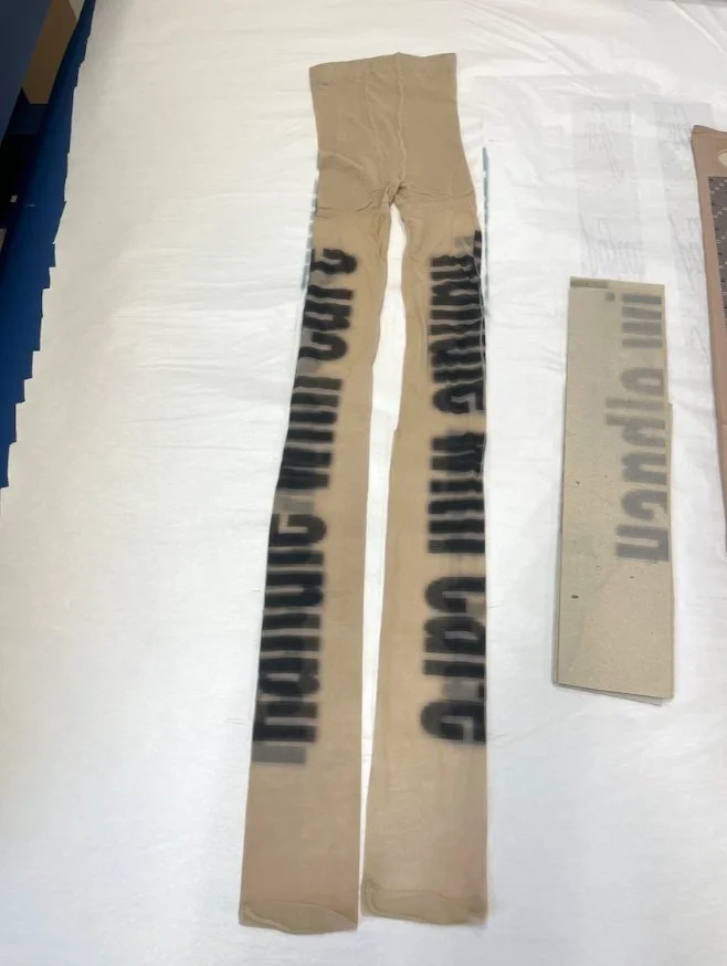 Flat lay of both-side printed nude tights with stenciled lettering, displayed on white background.