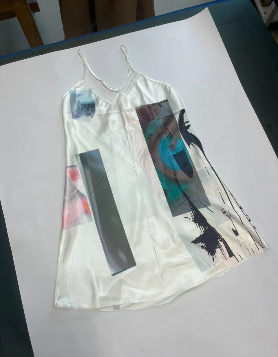 Flat lay of ivory satin dress featuring rectangular glitch prints, surgical hues, and muted scanline distortions
