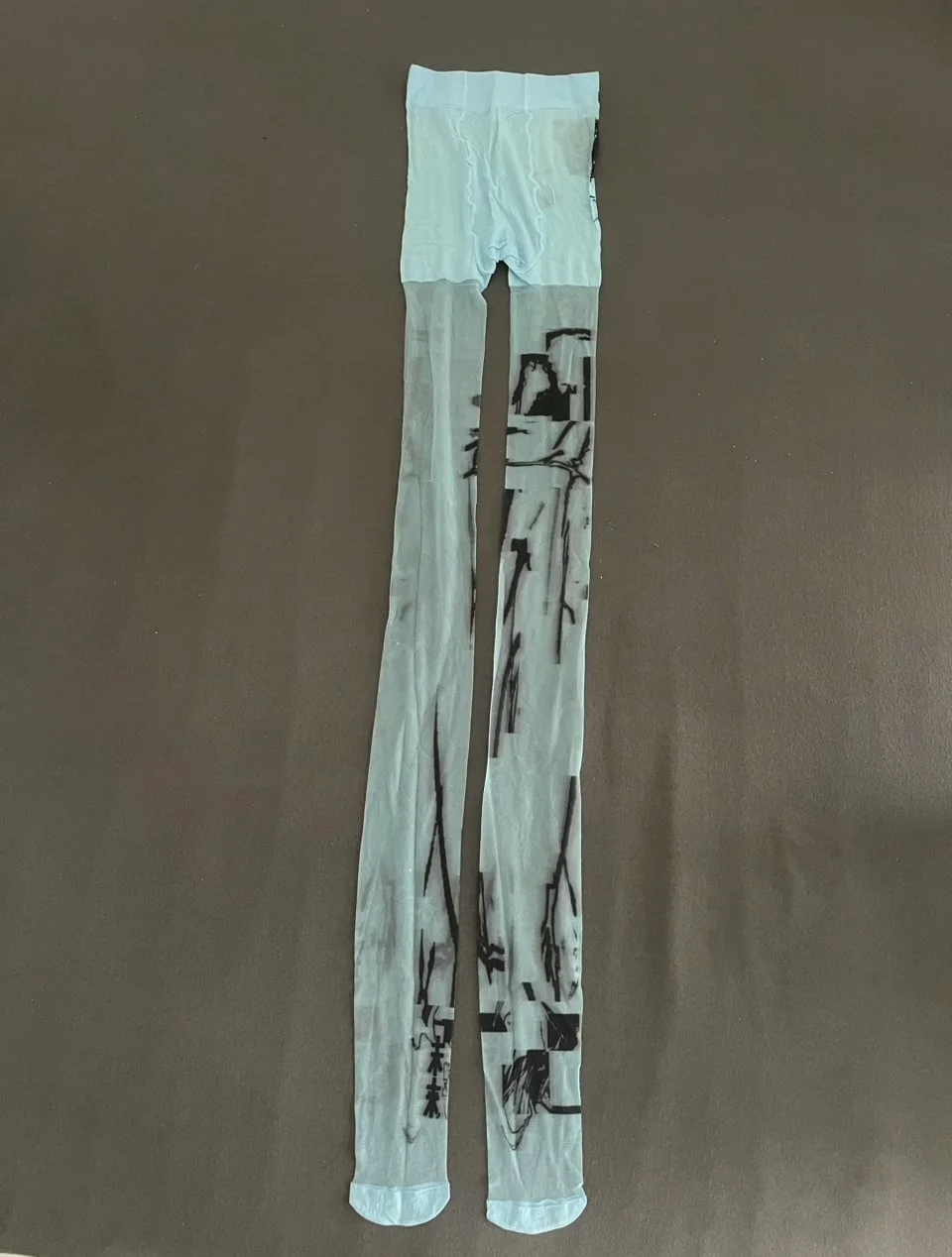 Back view of translucent mesh tights showing abstract black print and asymmetric detailing.