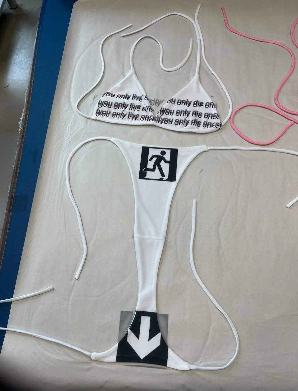 Graphic microkini in white featuring existential slogans and visual metaphors in minimal silhouette.